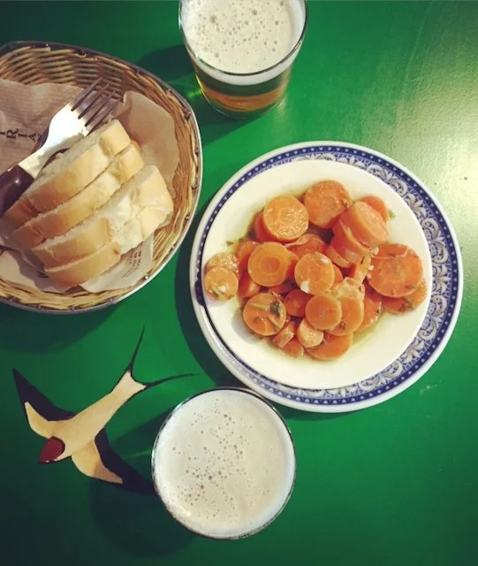 A tapas of marinated carrots with bread and a glass of beer