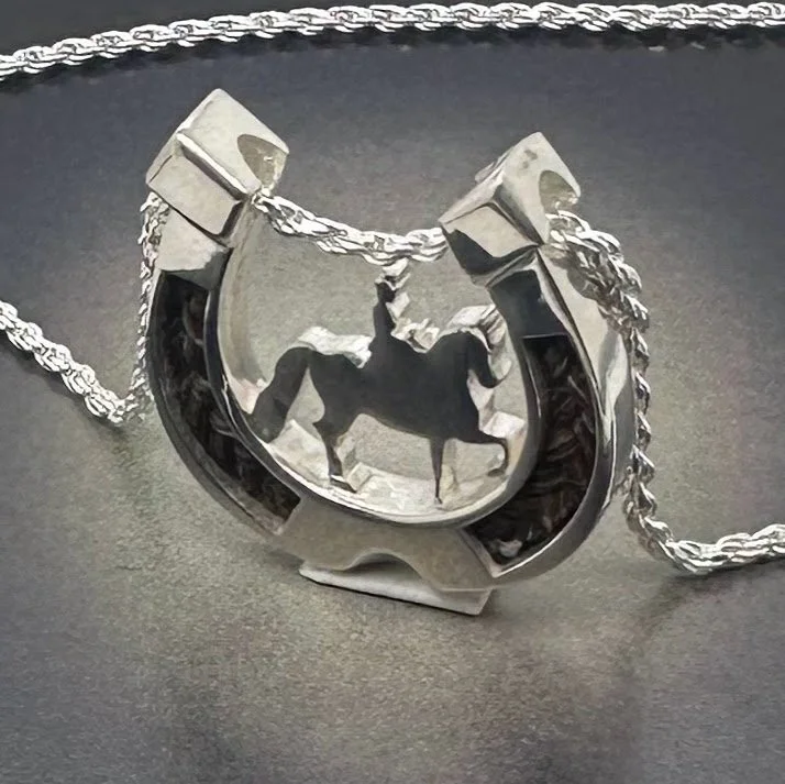 Angled view of handcrafted horseshoe pendant with raised sidesaddle rider silhouette and visible braided horsehair inlay.