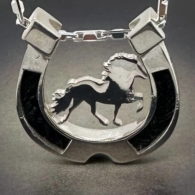 Backlit view of sterling horseshoe pendant showcasing Icelandic horse silhouette and braided horsehair inlay.