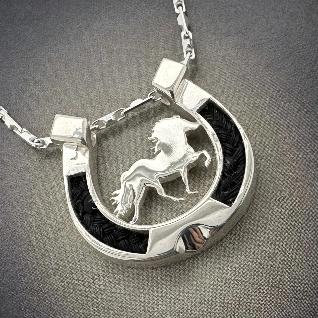 Close-up of handmade horsehair horseshoe necklace with Icelandic horse figure and textured chain.