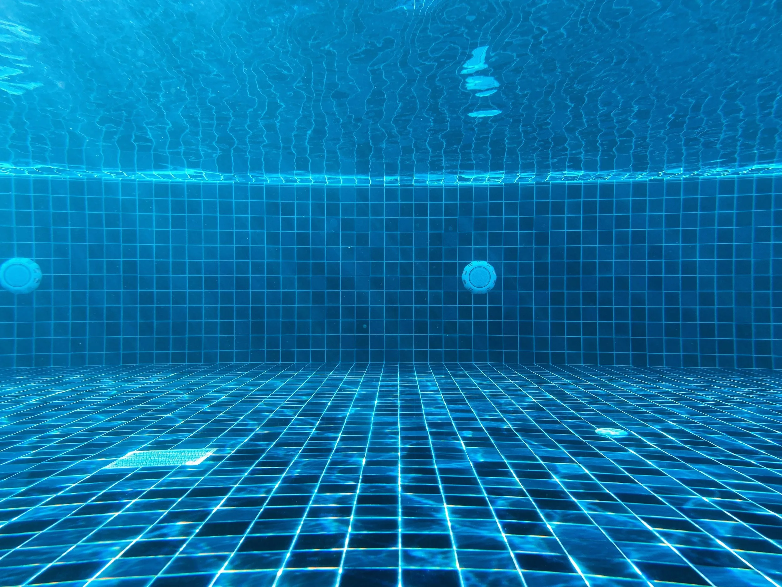 Blue tiled walls and floor of a swimming pool taken from perspective of someone sitting on the bottom of the pool, underwater