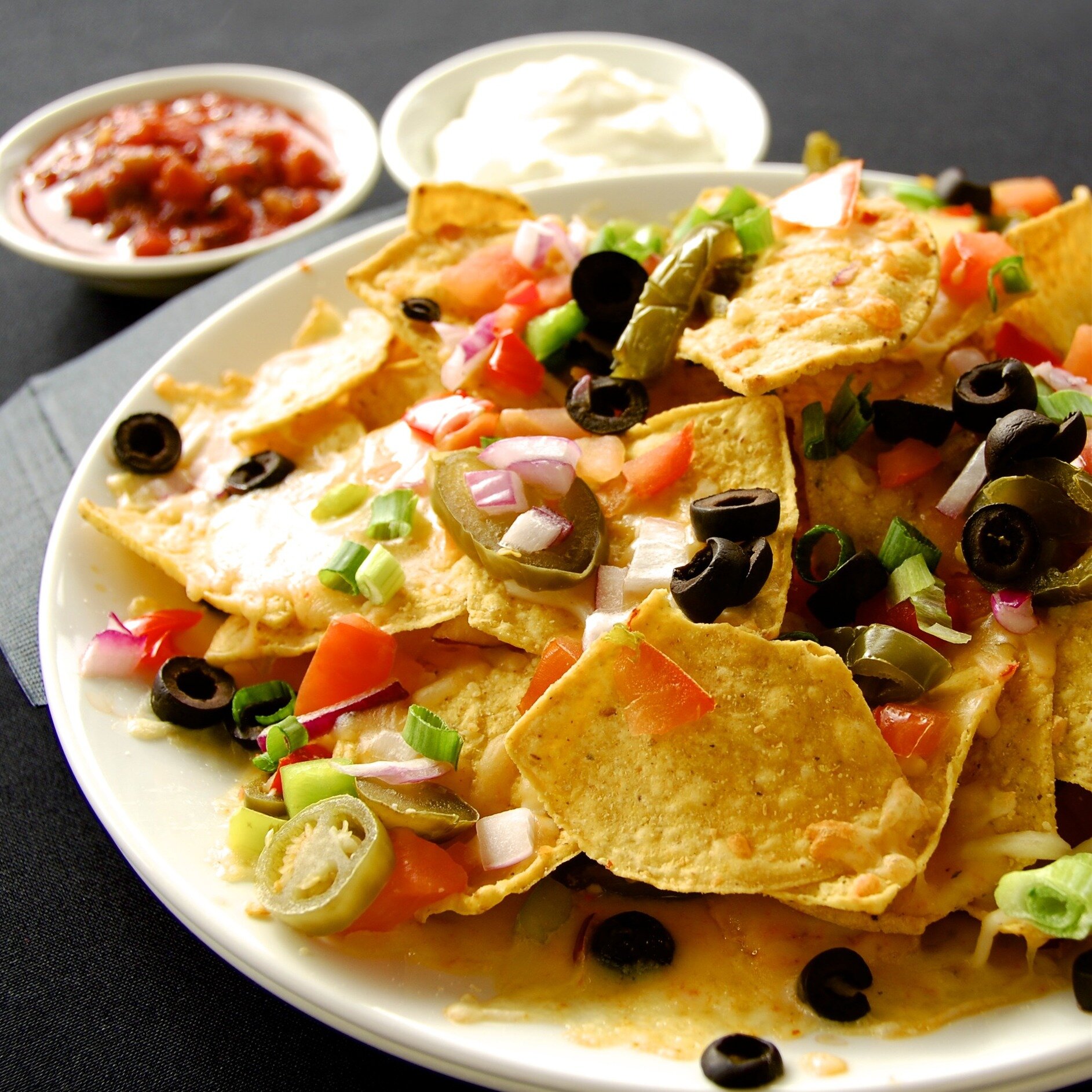 Join us for lunch or dinner and enjoy TC's Pub's popular Oven-baked Nachos! 
House-made chips oven baked with cheese and topped with jalape&ntilde;o, black olives, bell peppers, green onions &amp; tomatoes. Served with fire roasted salsa &amp; sour c
