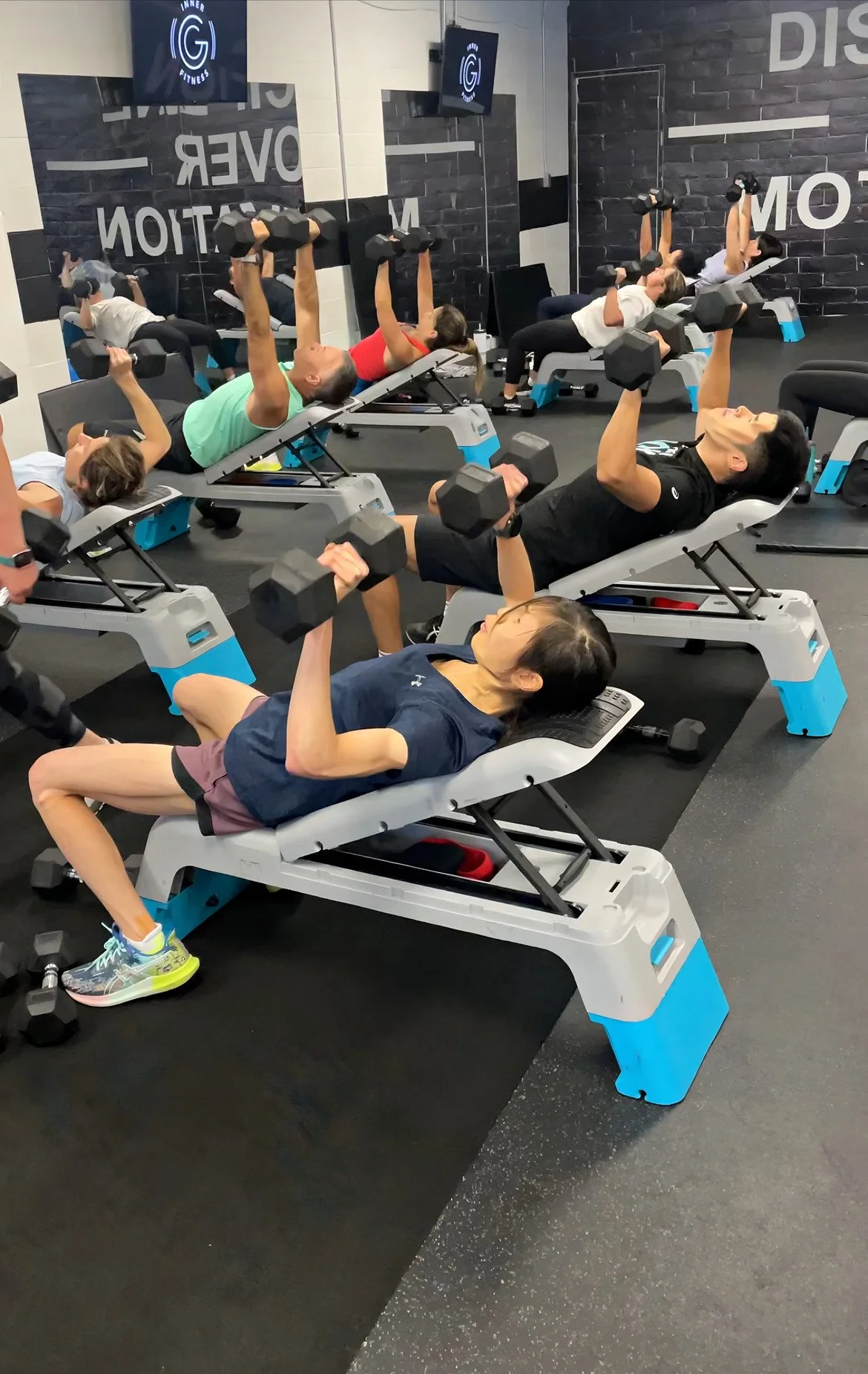 Members lifting dumbbells on benches in a small-group class at Inner G