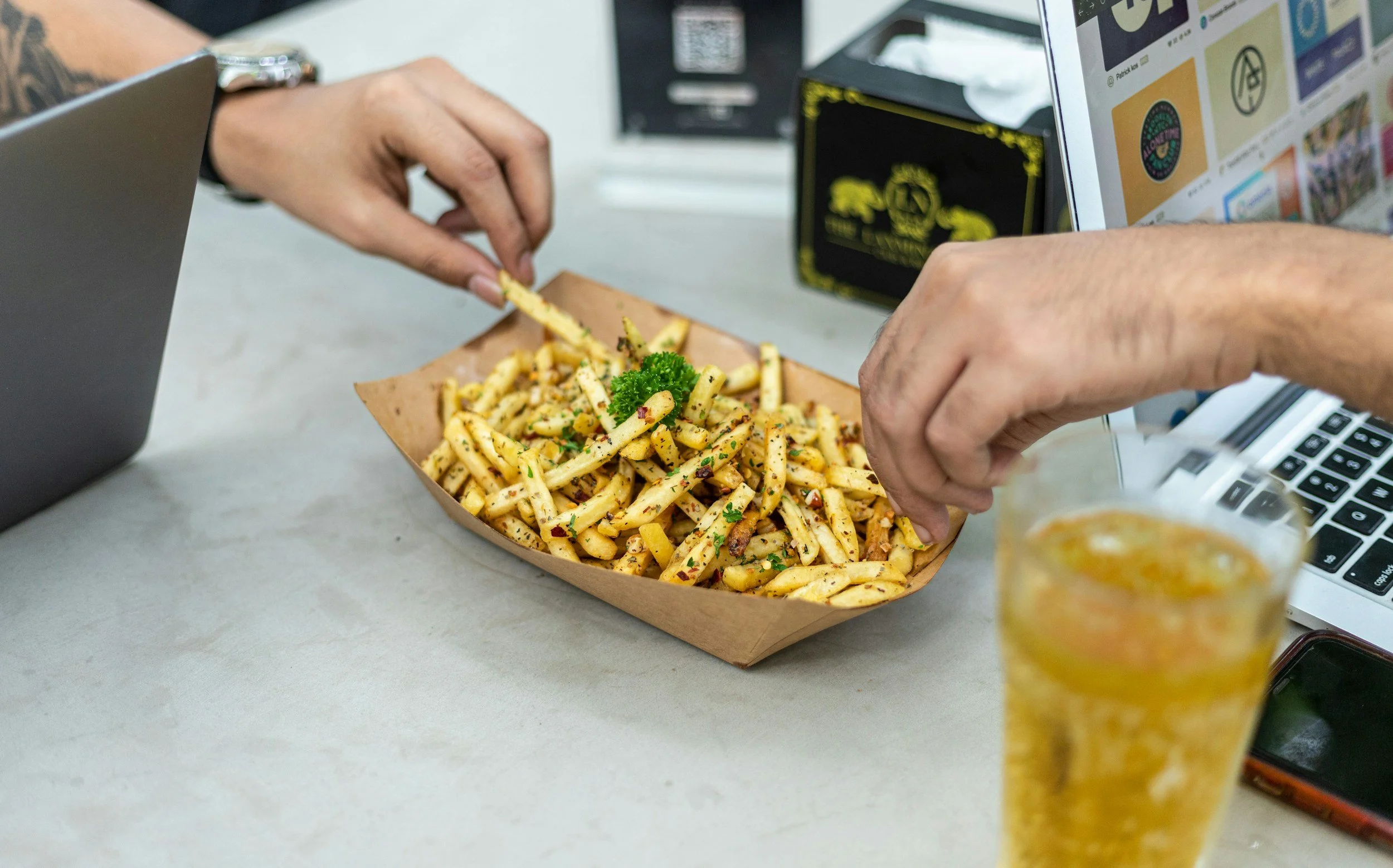 Two hands grabbing fries out of one basket.