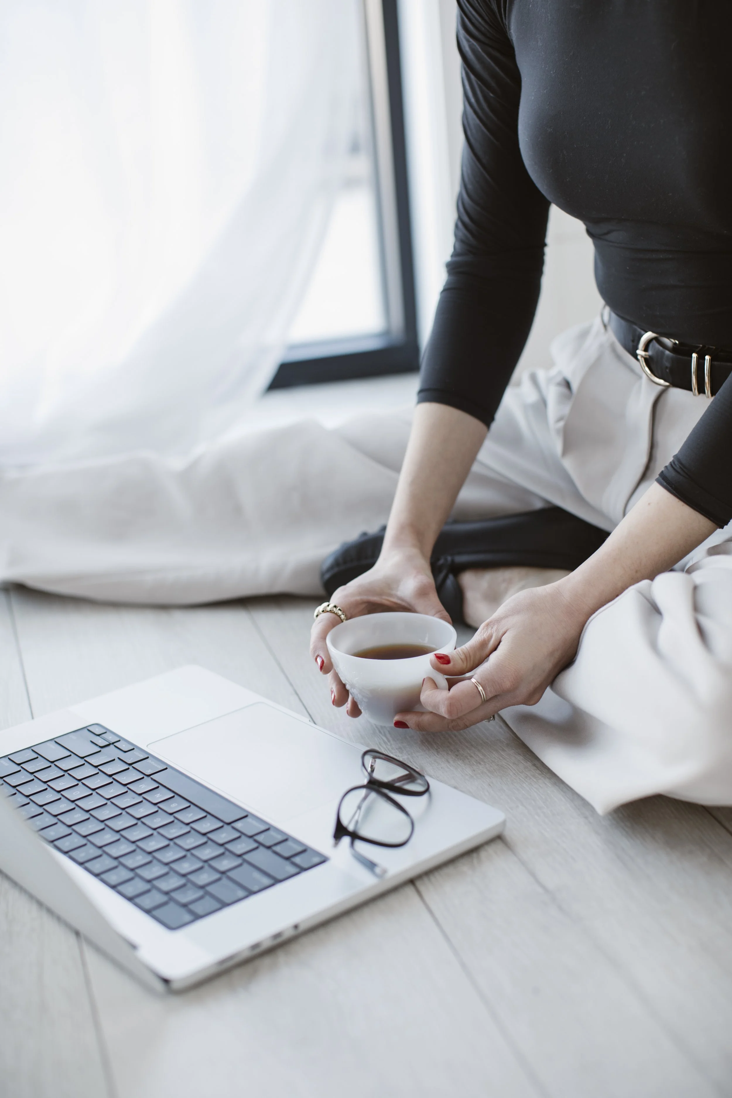 Shyanne Reynolds sitting on the floor holding a cup of coffee, a laptop open in front of her.