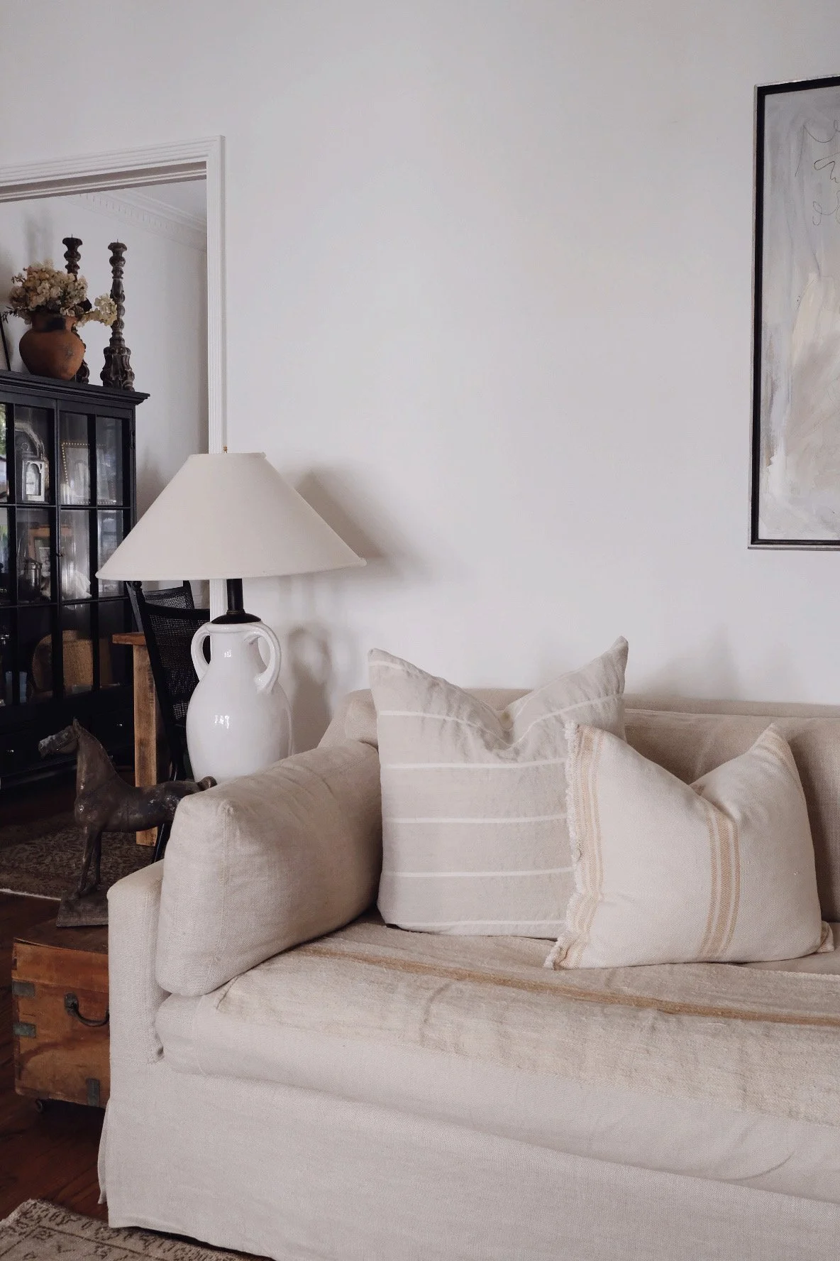 French linen couch with accent cushions and pillows, antique ceramic white table lamp and antique rustic wood furniture side table