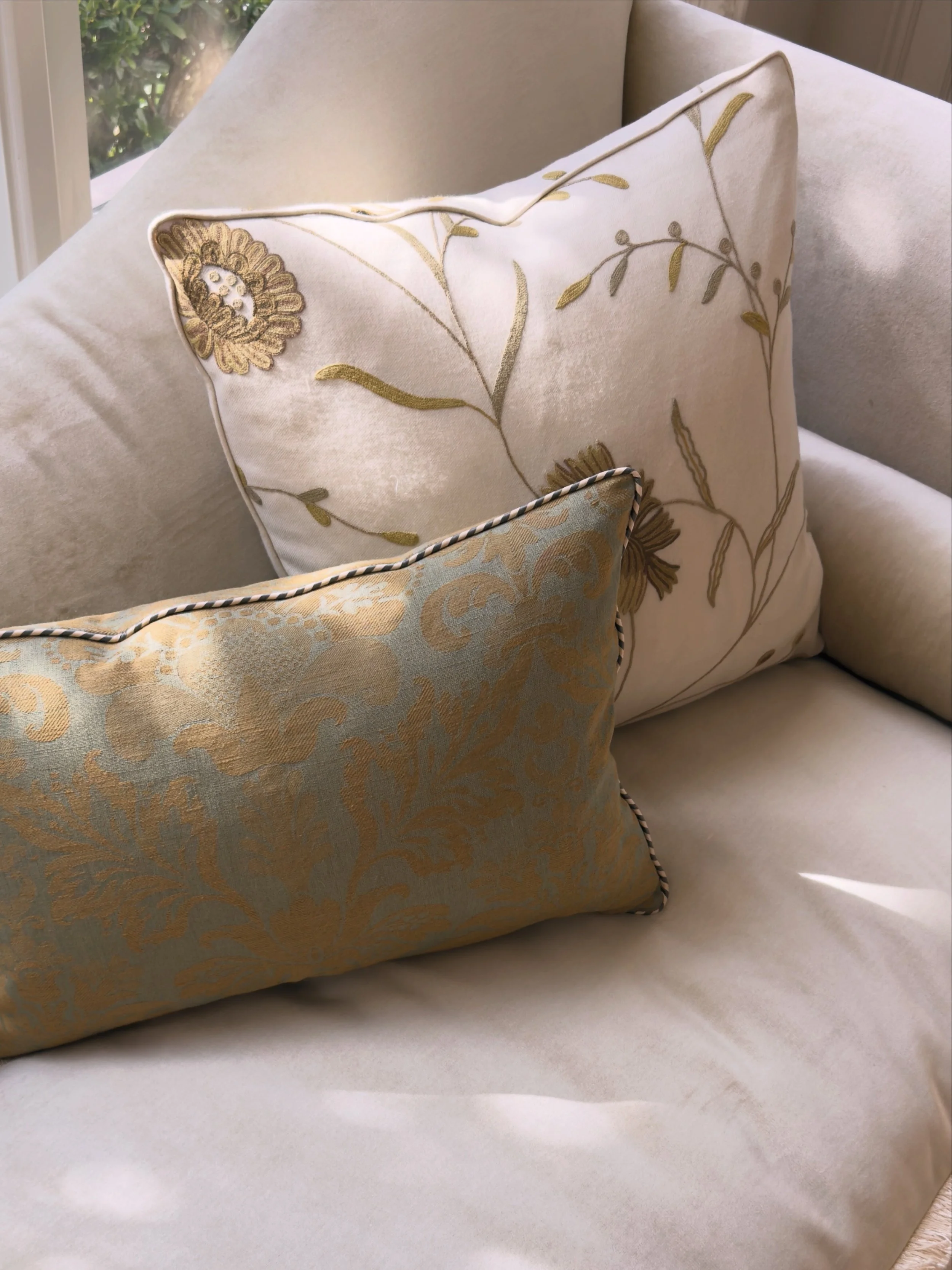 CIËN Interiors – antique wool crewel embroidered linen, pillow, and silk down, lumbar with twisted cord piping on an ivory velvet sofa