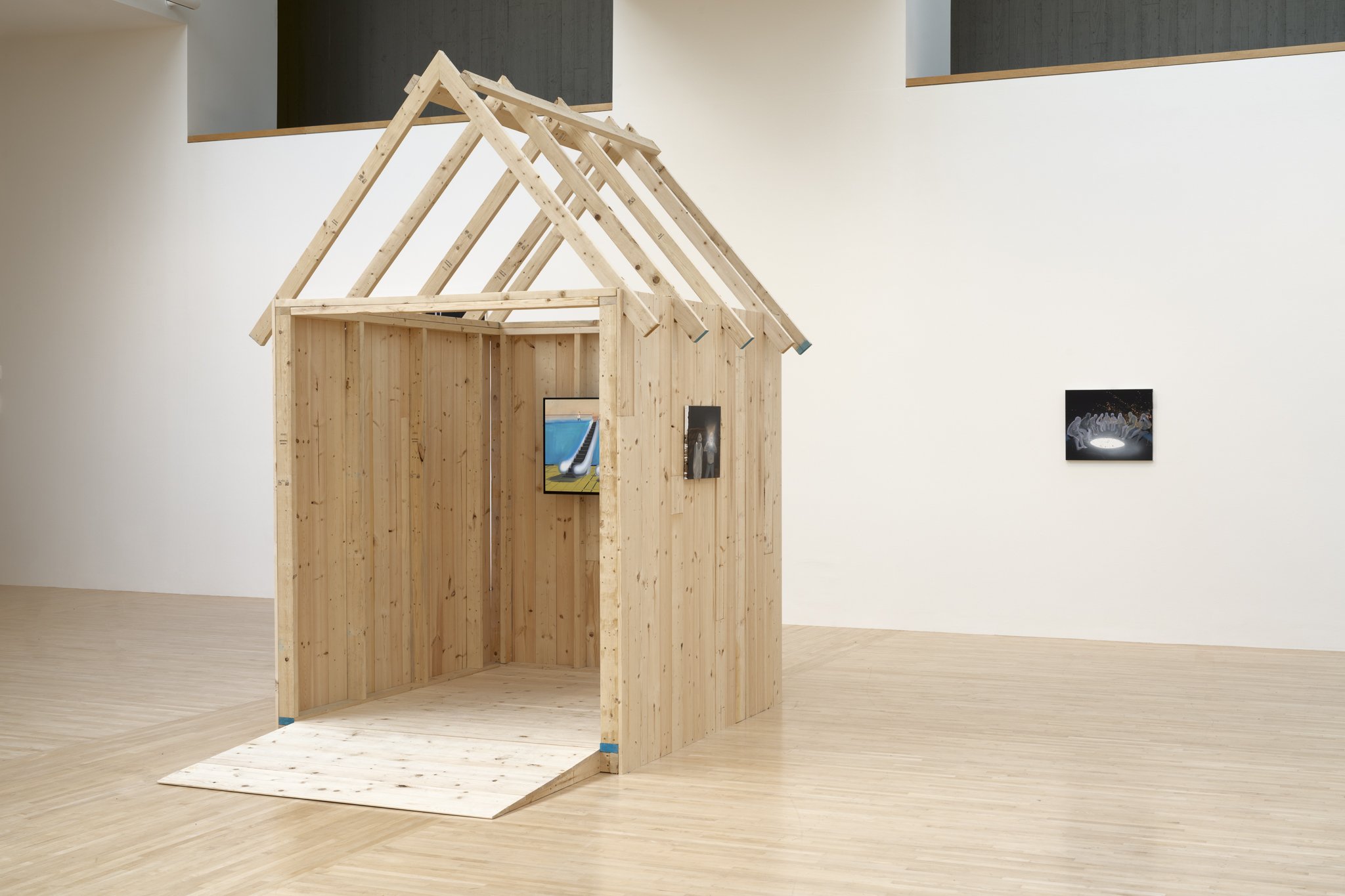 a wood shed with video screen and paintings in a gallery