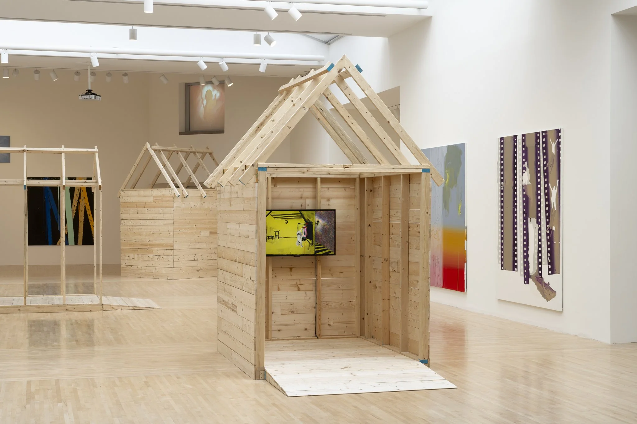 wood sheds with video screens and paintings in a gallery