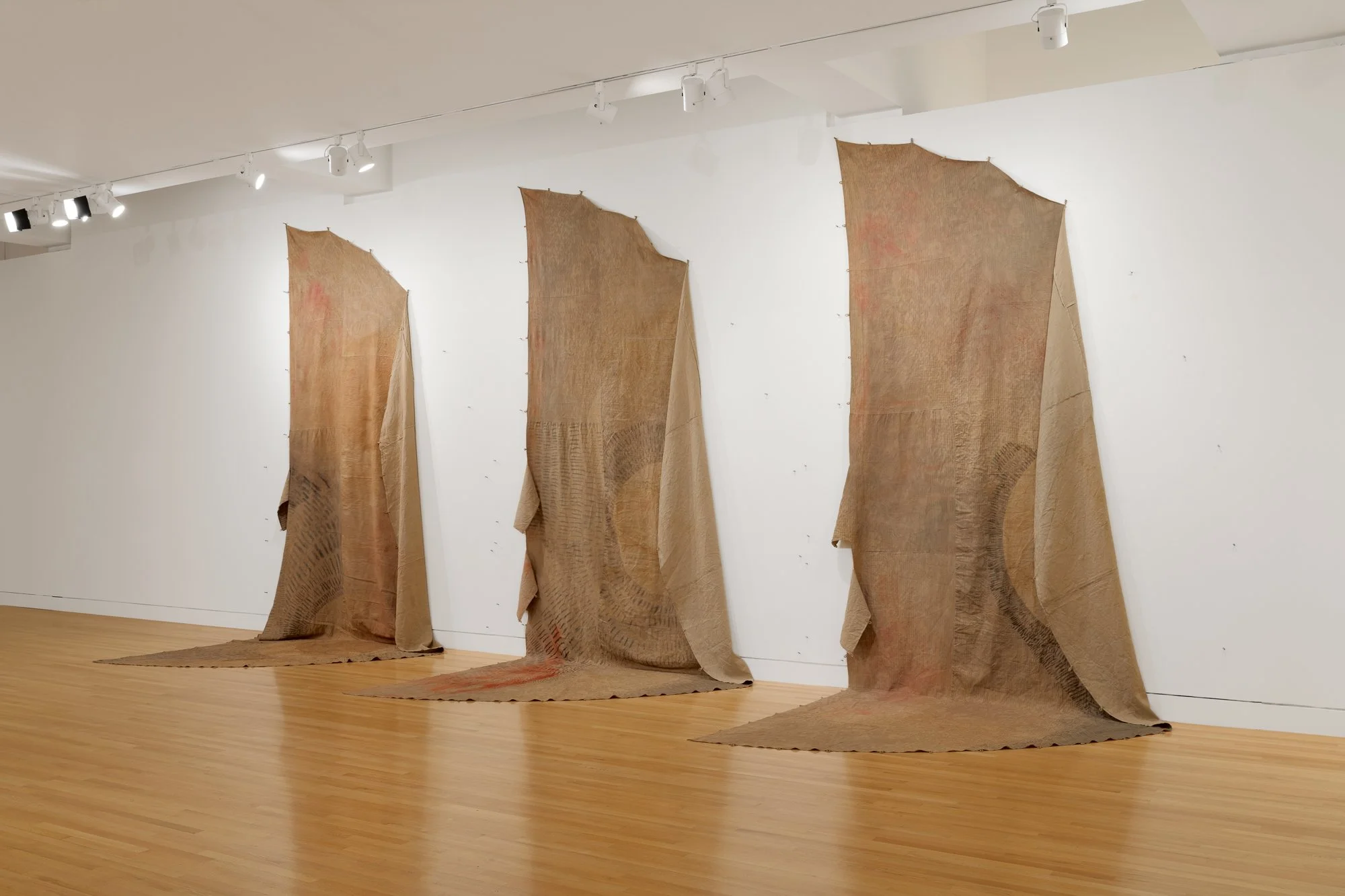 three textile works on the wall in the shape of teepee covers