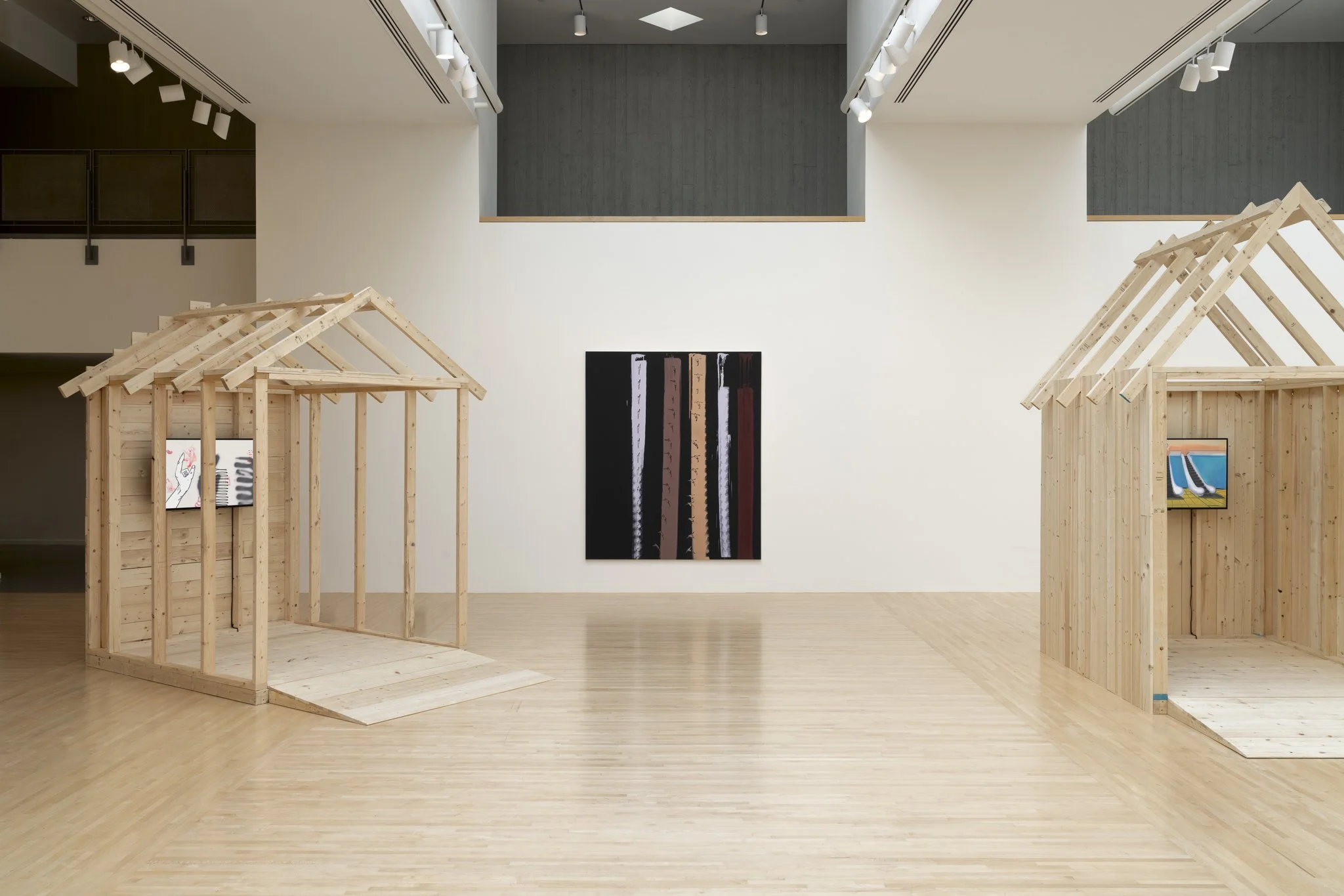 wood sheds with video screens and paintings in a gallery