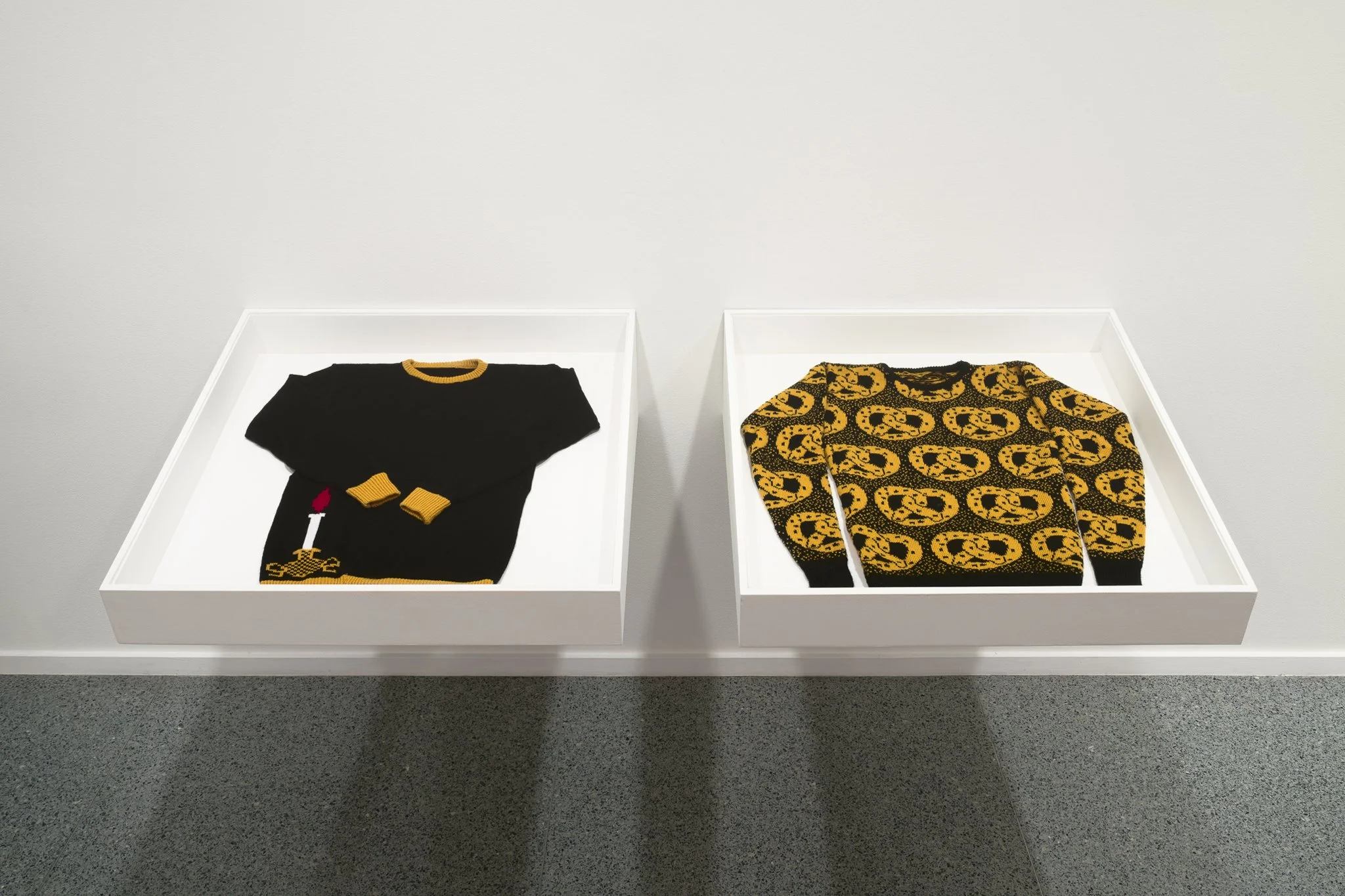 two sweaters in plexi boxes on the wall