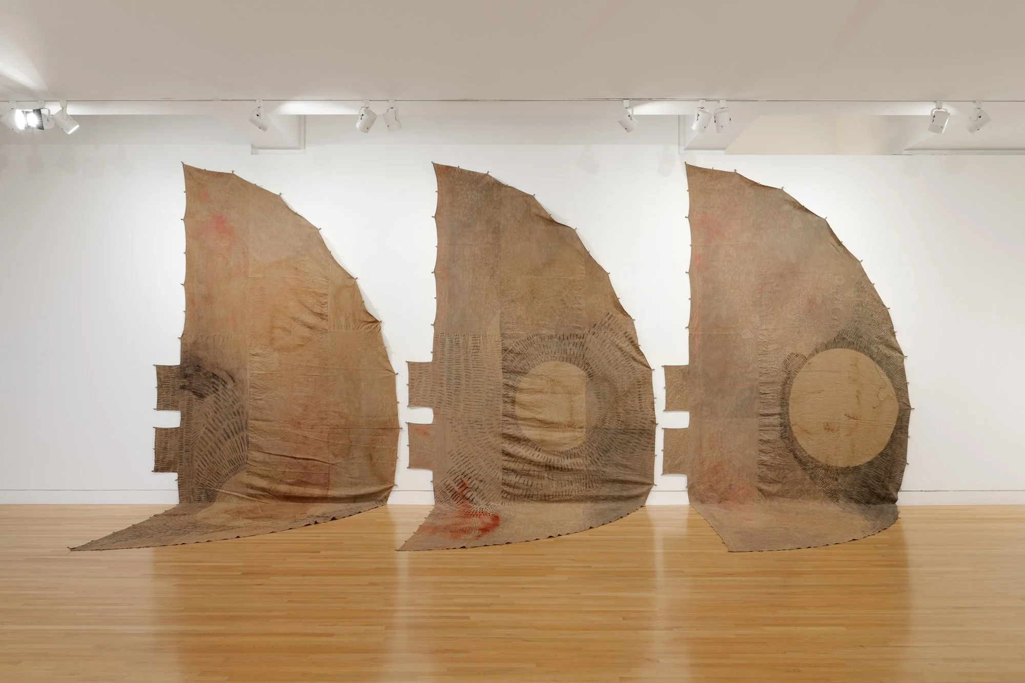 three textile works on the wall in the shape of teepee covers