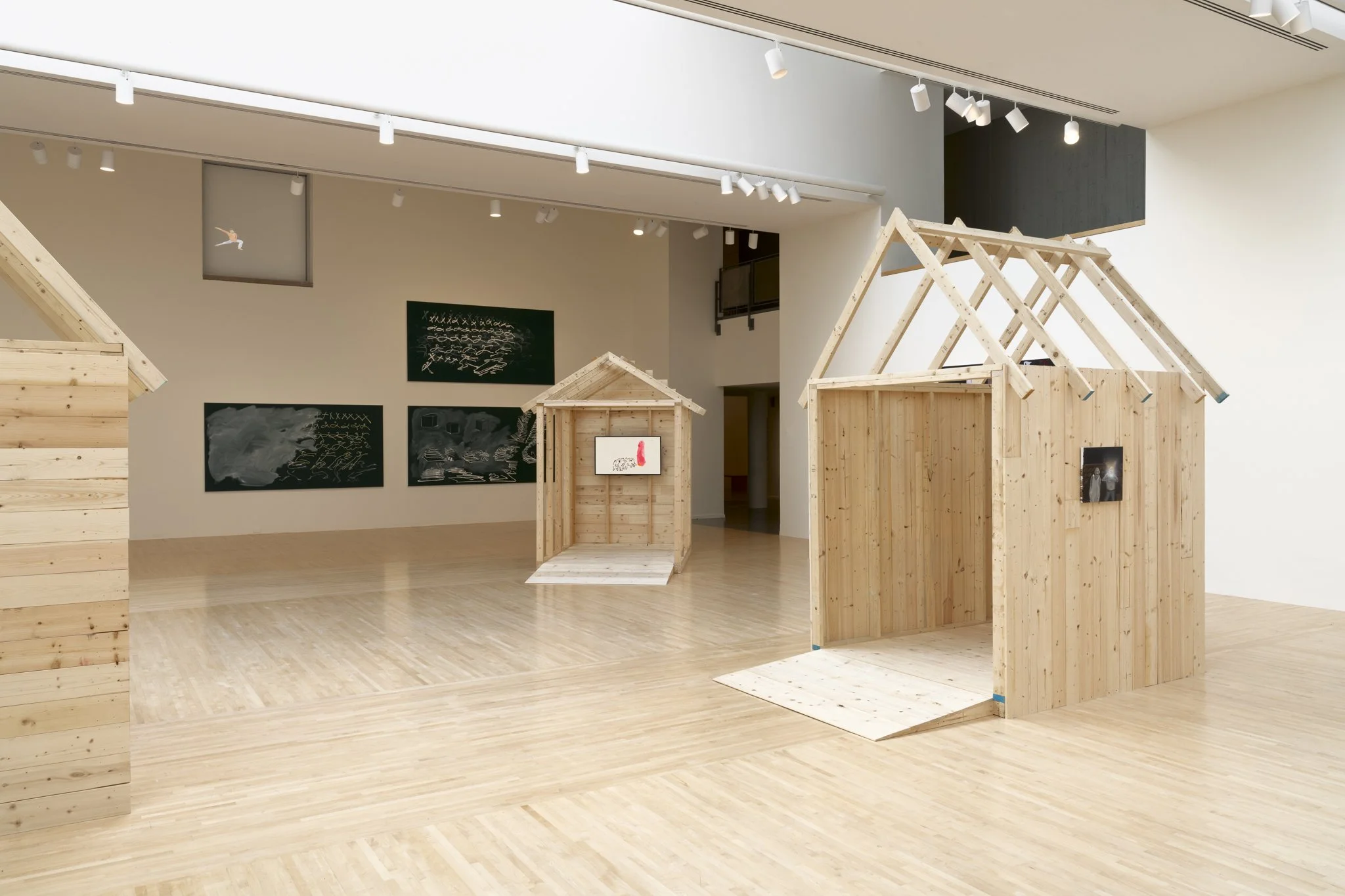 wood sheds with video screens and paintings in a gallery