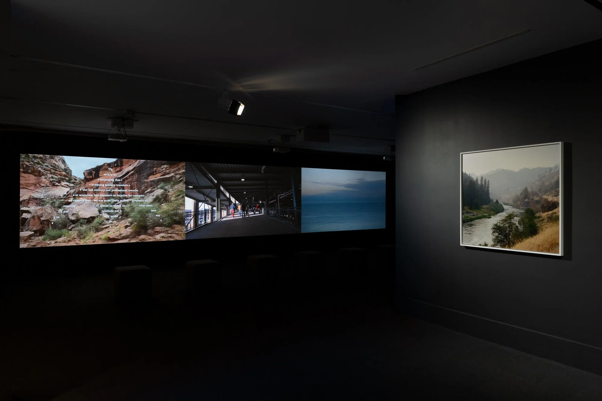 a framed photo and three projected videos in a black gallery