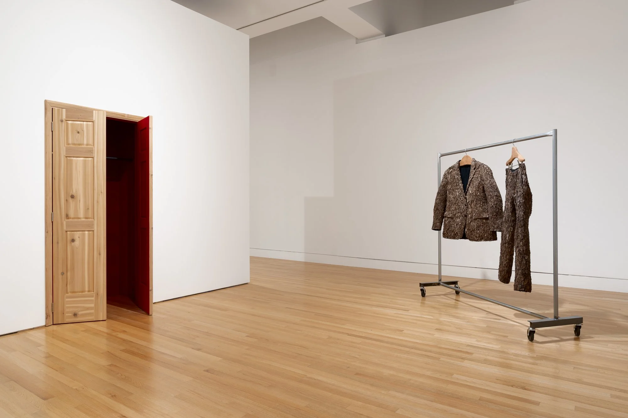 an open door on the left; a clothes rack with garments made of tree barks on the right