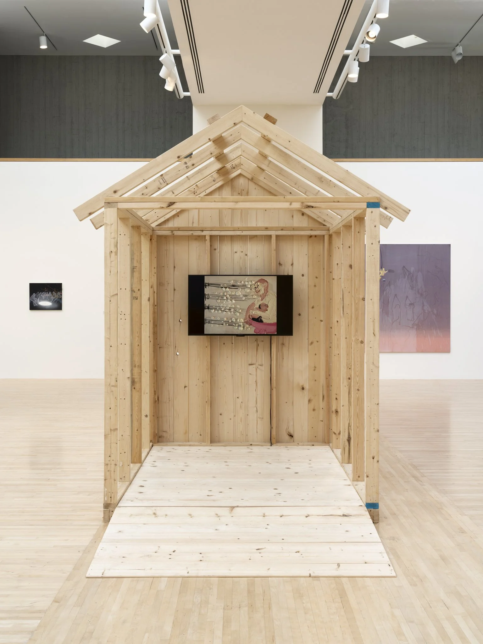 a wood sheds with a video screen and paintings in a gallery