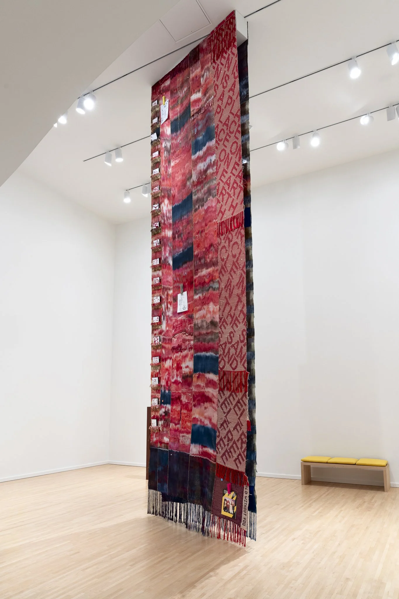 a large red textile piece hung in a gallery with tall ceiling