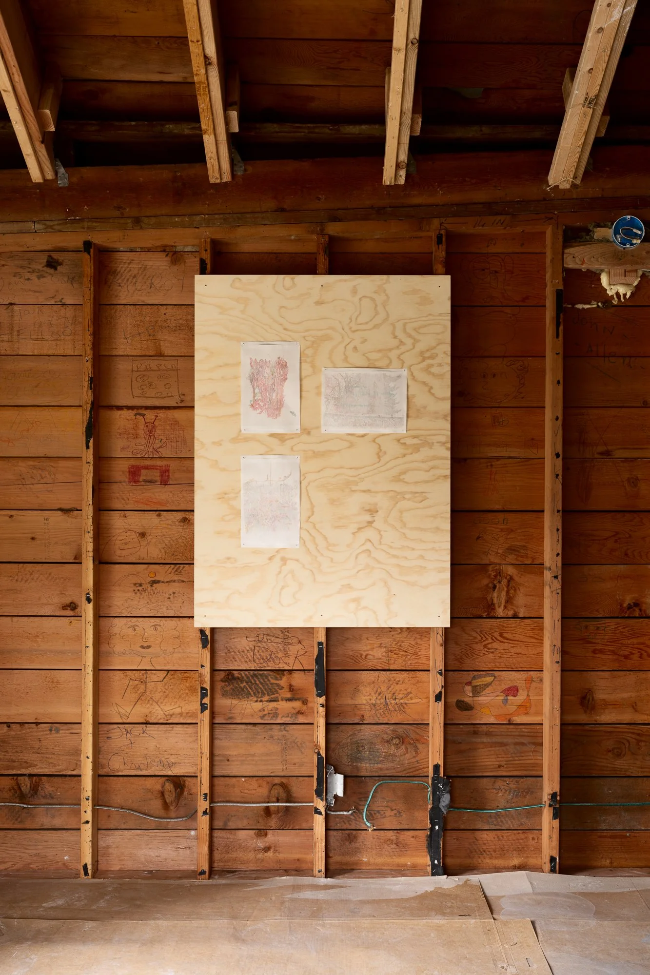 3 drawings on a piece of plywood attached to bare studs