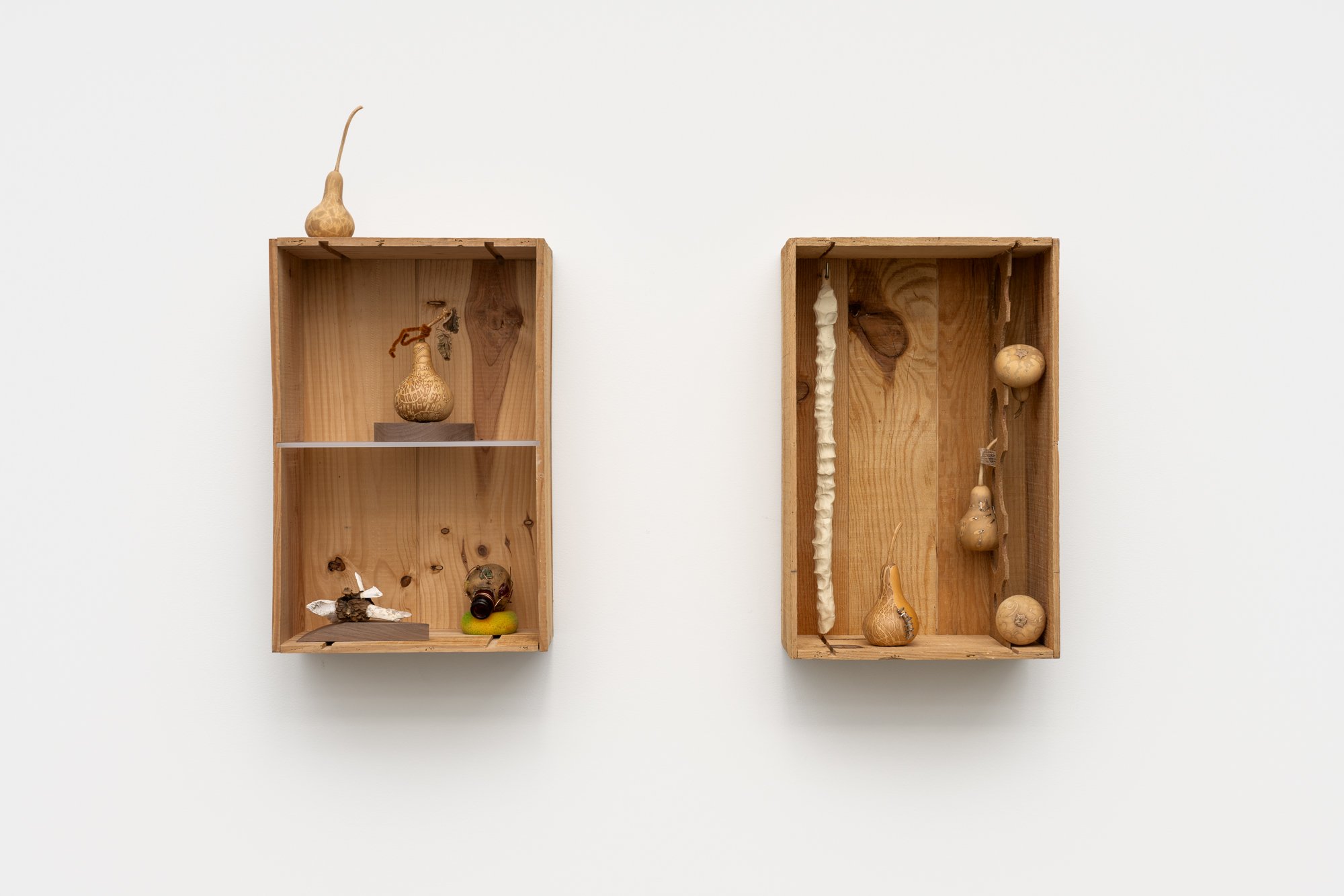 two wooden boxes on a white wall, with sculptures inside
