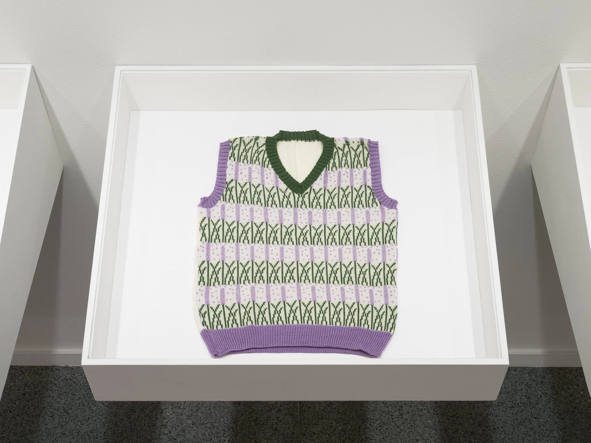 a sweater with green and purple patterns in a plexi box