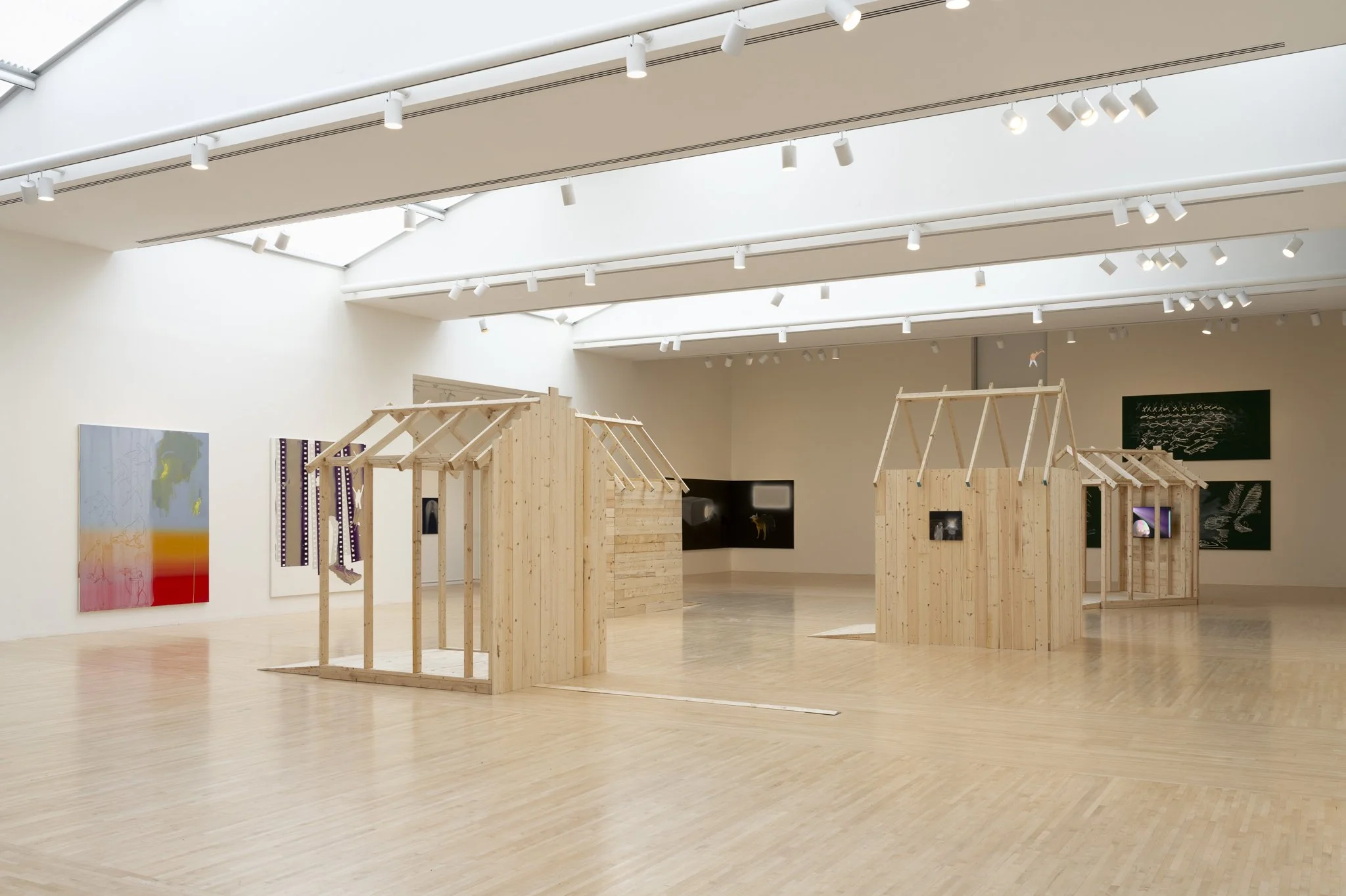 wood sheds with video screens and paintings in a gallery