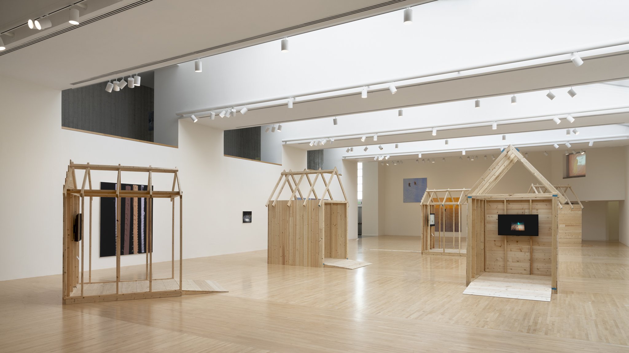 wood sheds with video screens and paintings in a gallery