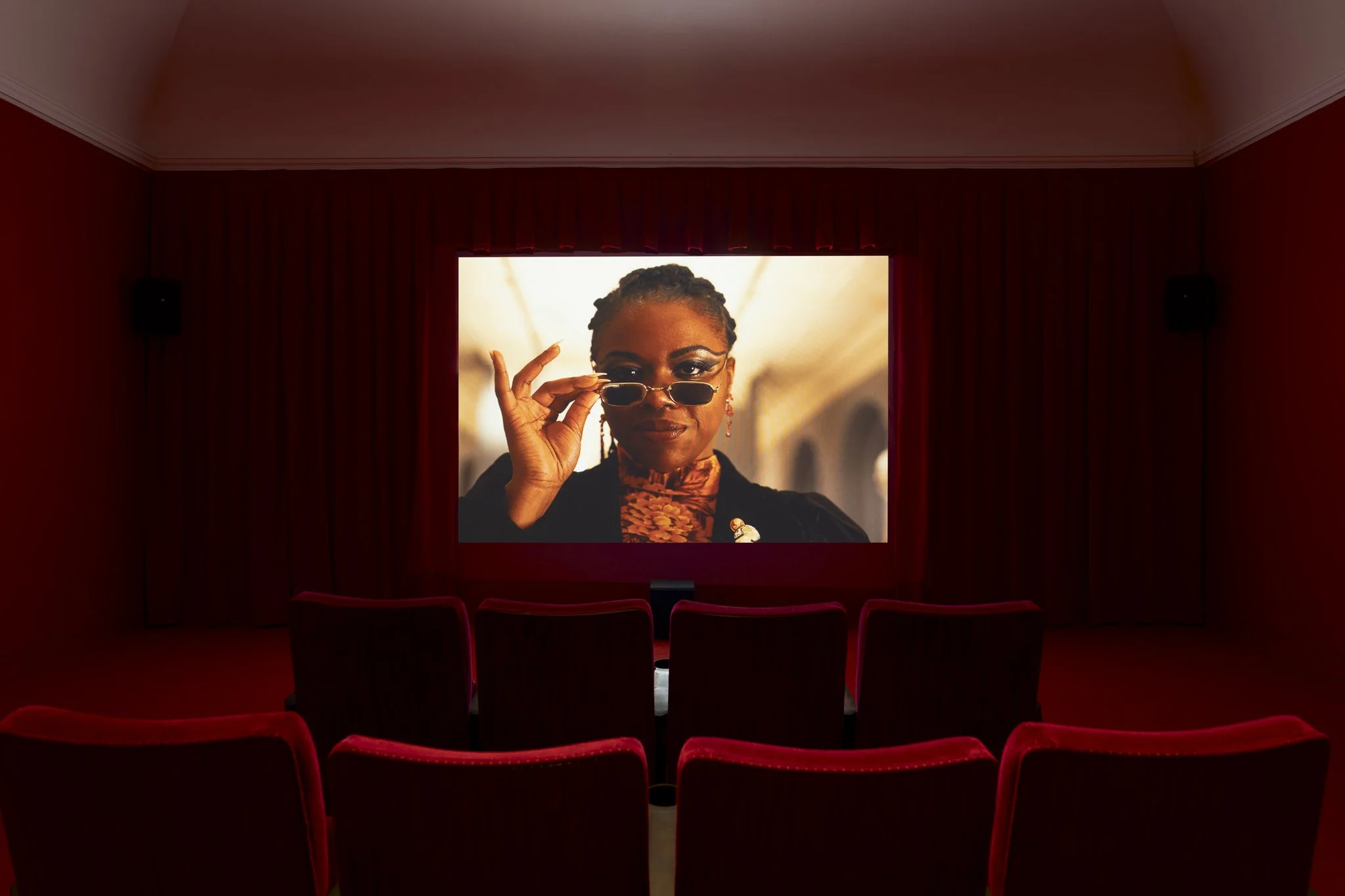 a video in a red theater showing a woman holding sunglasses