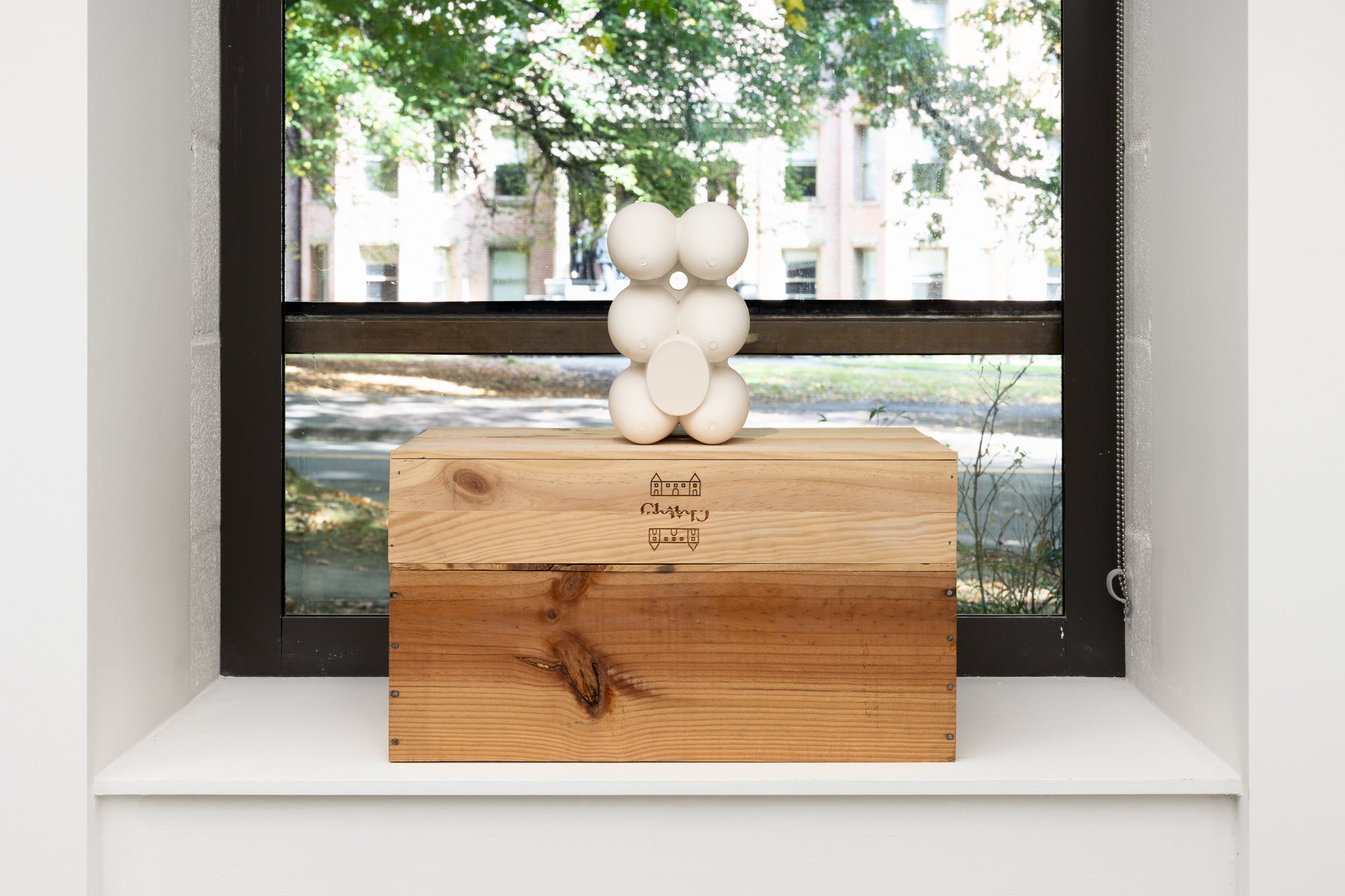 a white sculpture sitting on a wooden box on the window sill