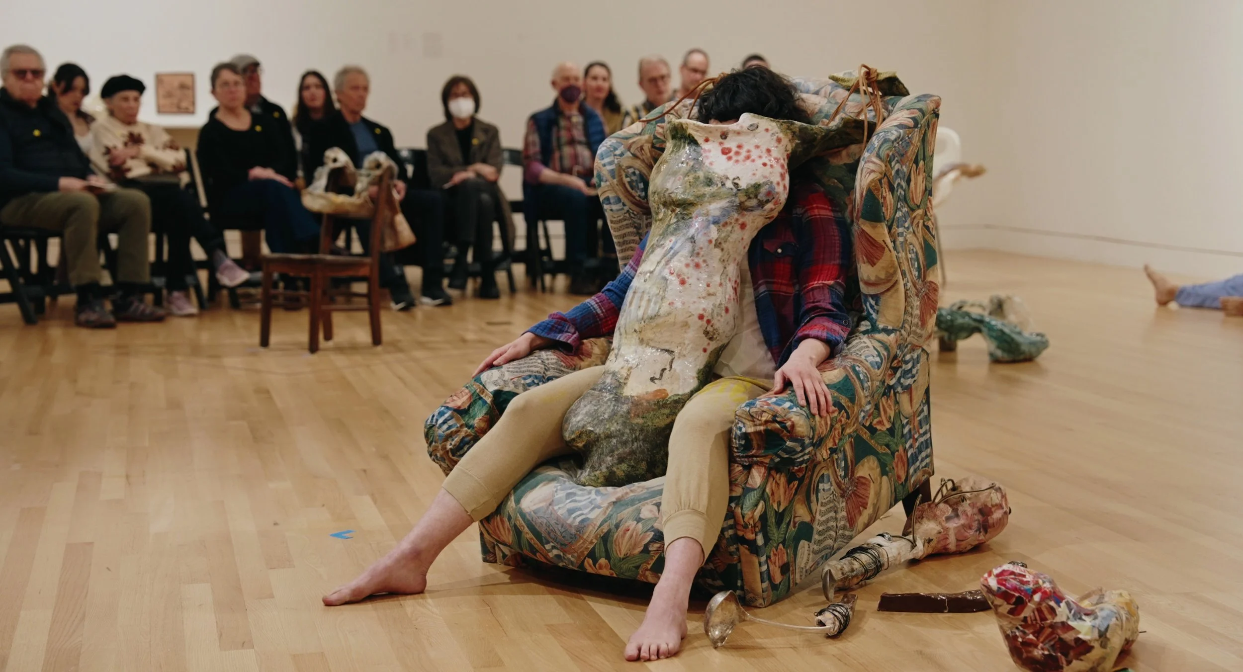 a performer wearing a ceramic sculpture sitting in a chair