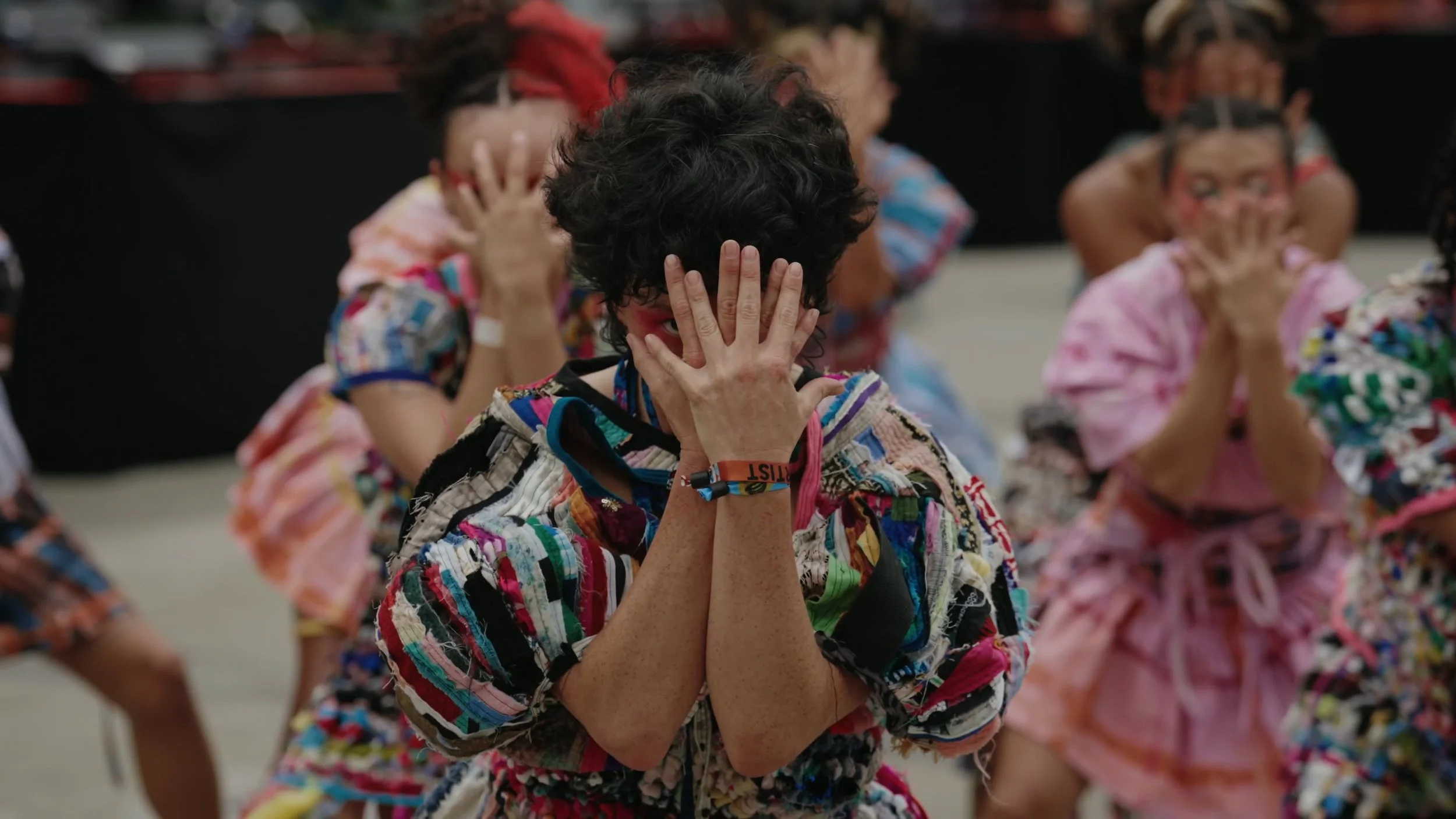 dancers in colorful garments covering their faces with their hands