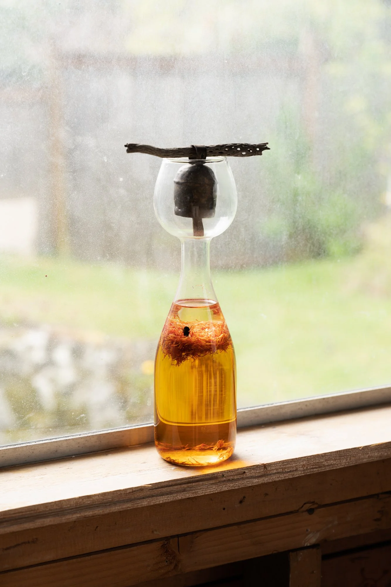 a sculpture made of a glass vessel, orange liquid, and a bell