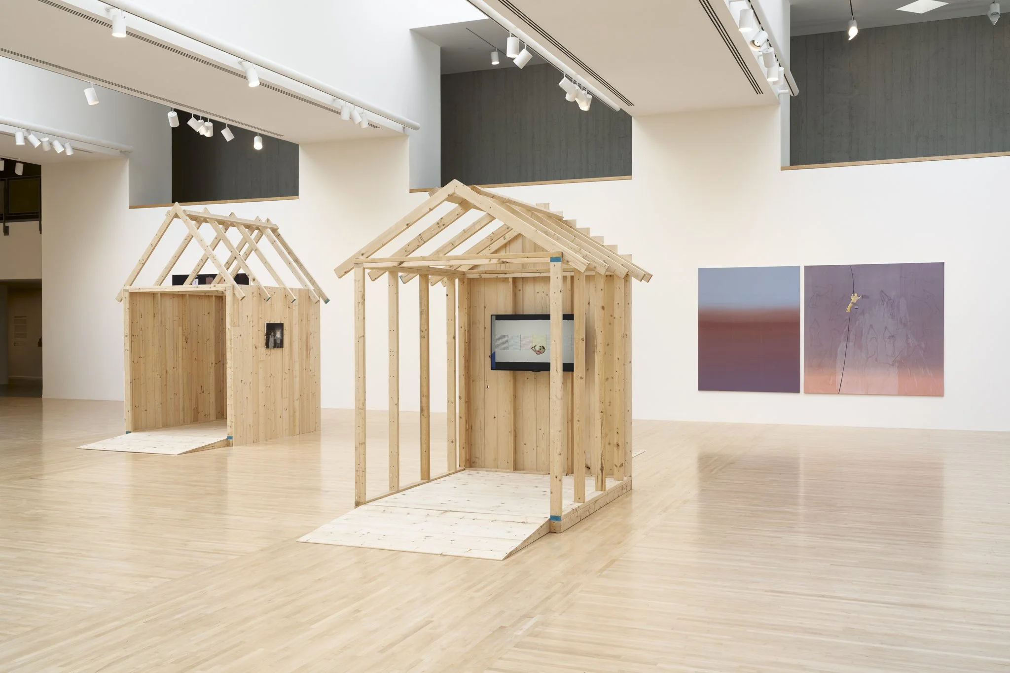 wood sheds with video screens and paintings in a gallery