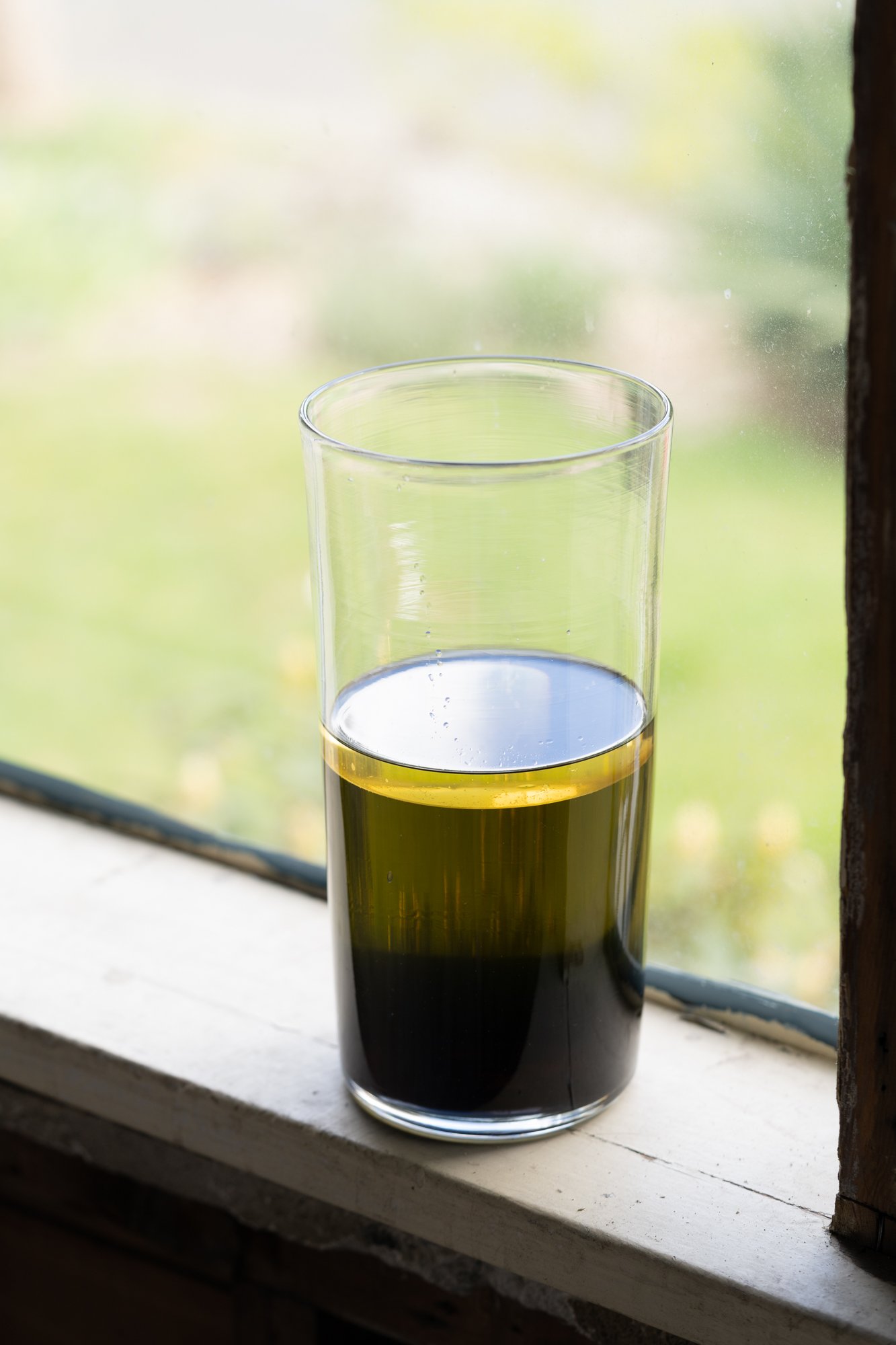 a glass vase with green liquid on a window sill