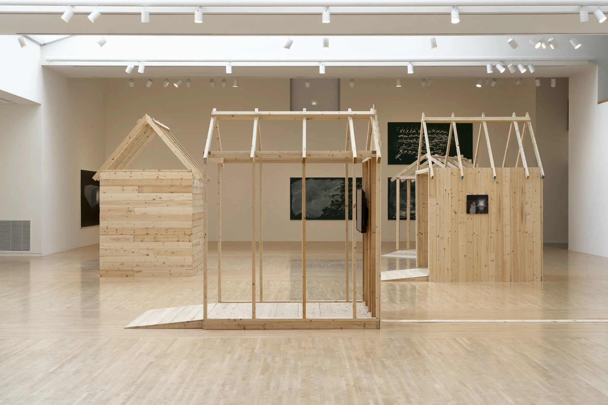 wood sheds with video screens and paintings in a gallery