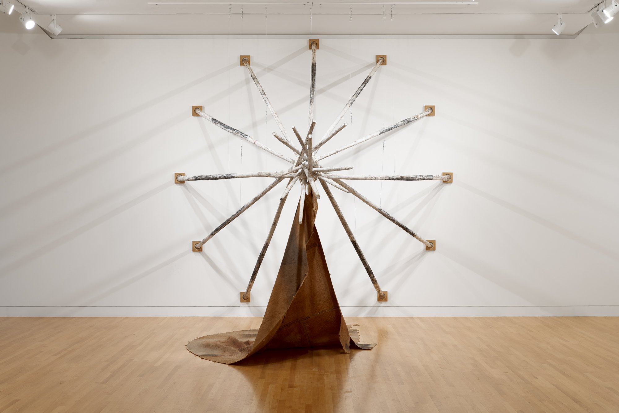 a large sculpture made of wood poles in teepee shape and a textile