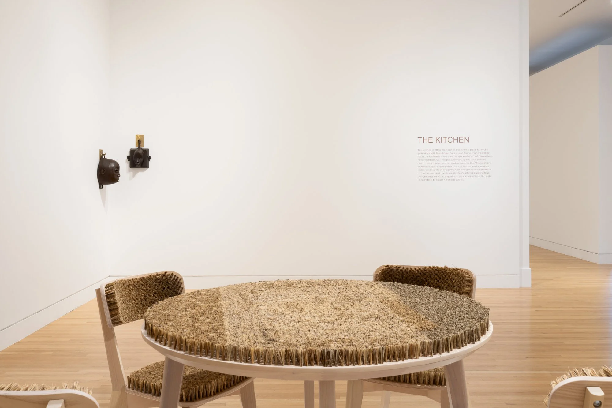 in the foreground, a table with 4 chairs, all with brushes as the top surface; in the background, two cast iron pans in the shapes of masks