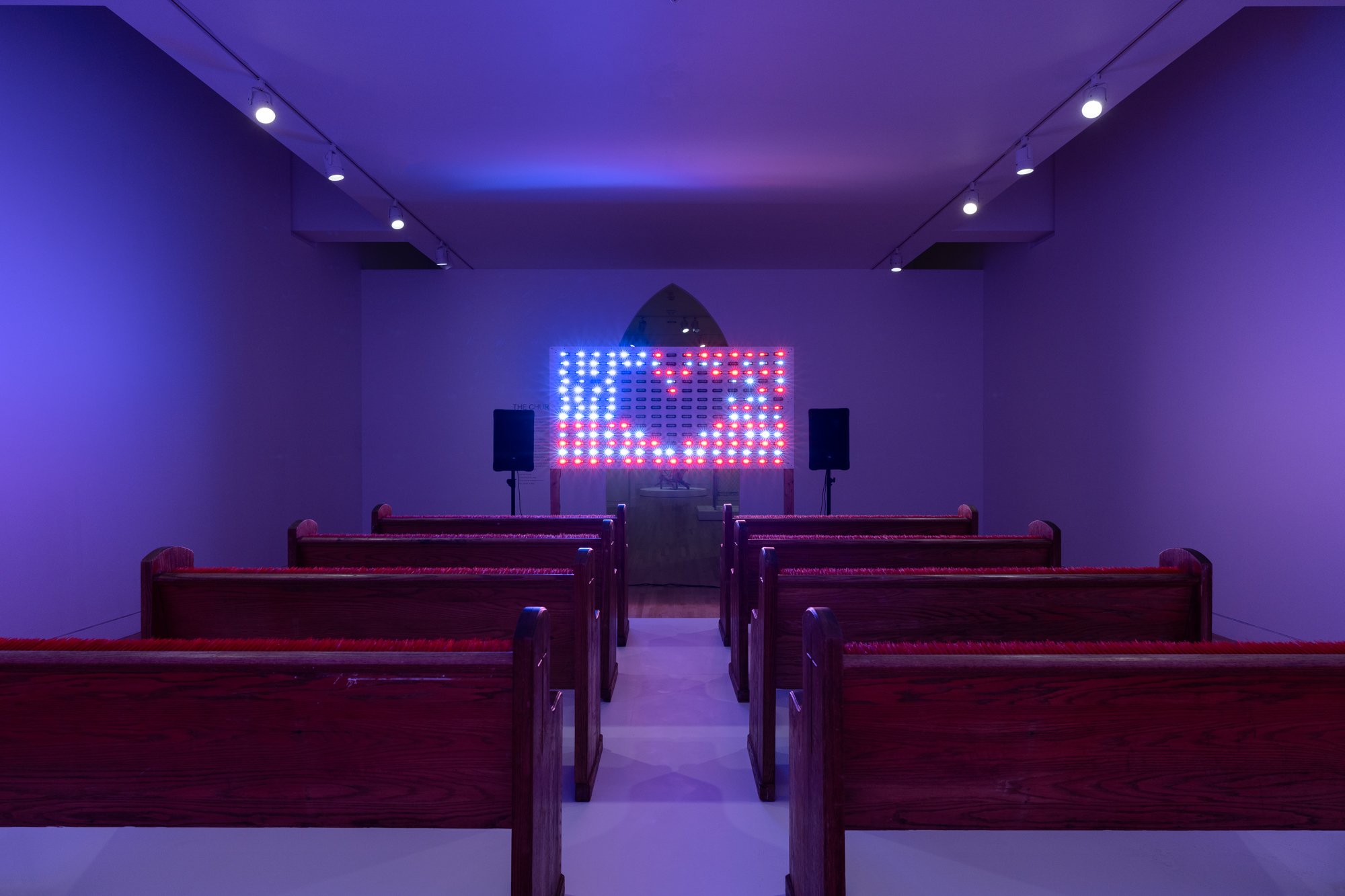 an LED panel showing a heart shape on an american flag in front of church pews
