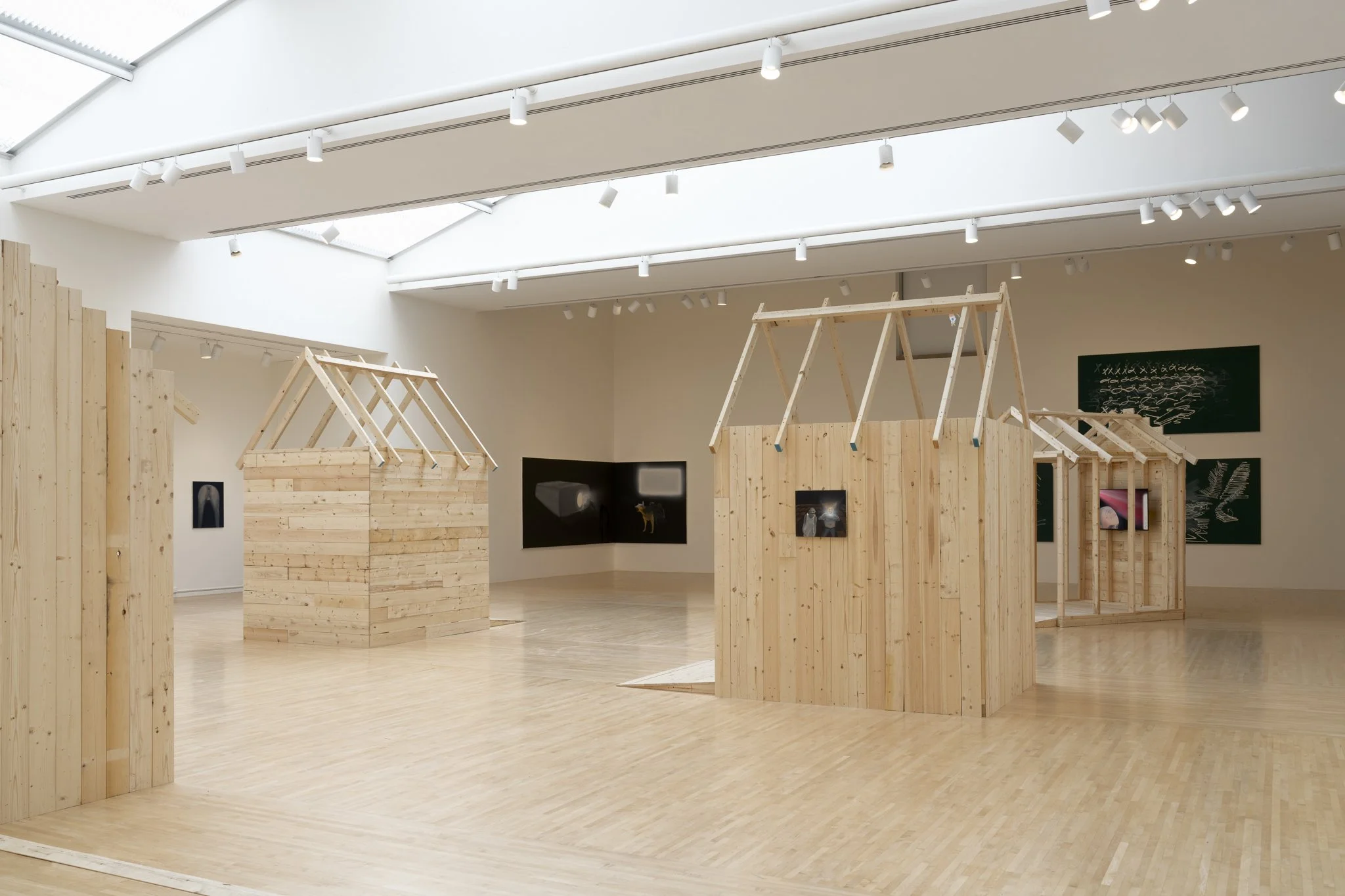wood sheds with video screens and paintings in a gallery