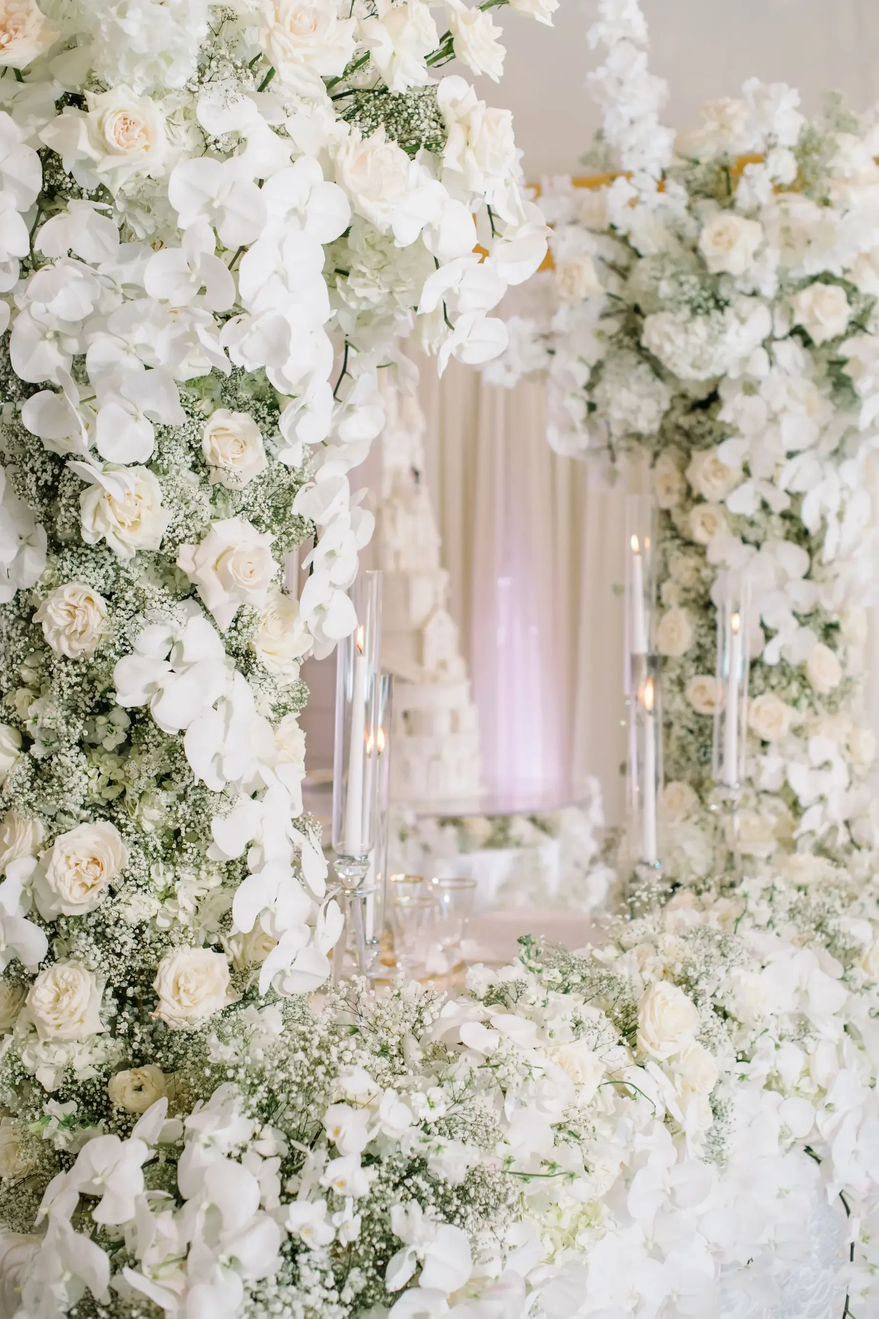 A wedding altar decorated with white flowers including roses, orchids, and baby's breath, with tall candles in glass holders.