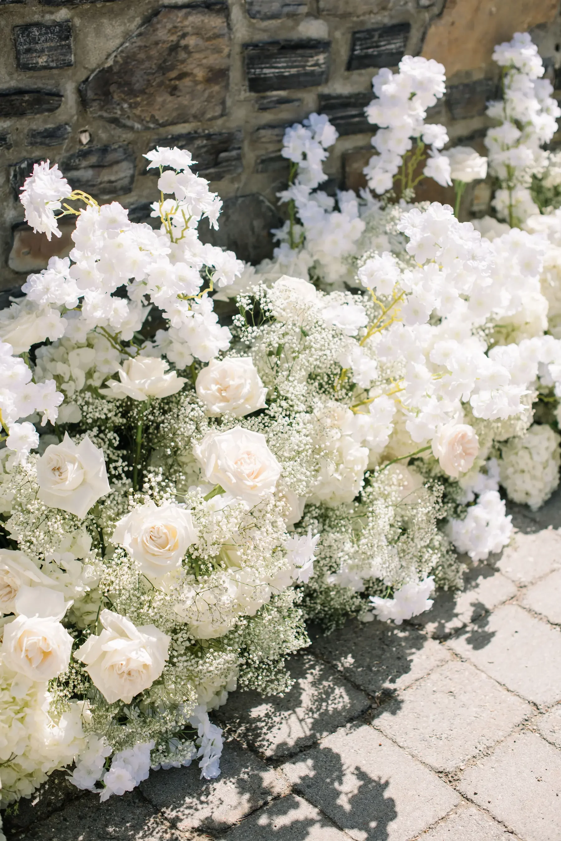 White flowers and roses arrangement leaning against a brick wall on a paved surface.