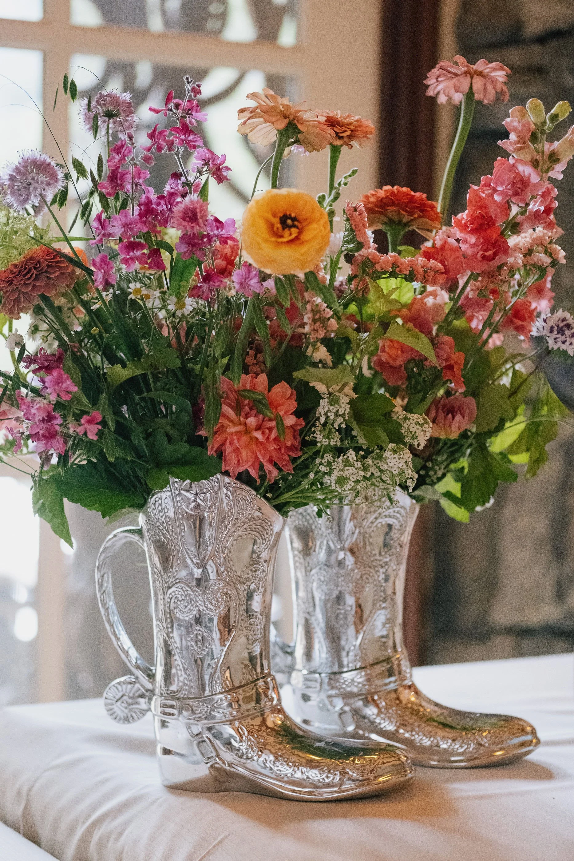 A bouquet of colorful flowers in clear cowboy boot vases on a table indoors.