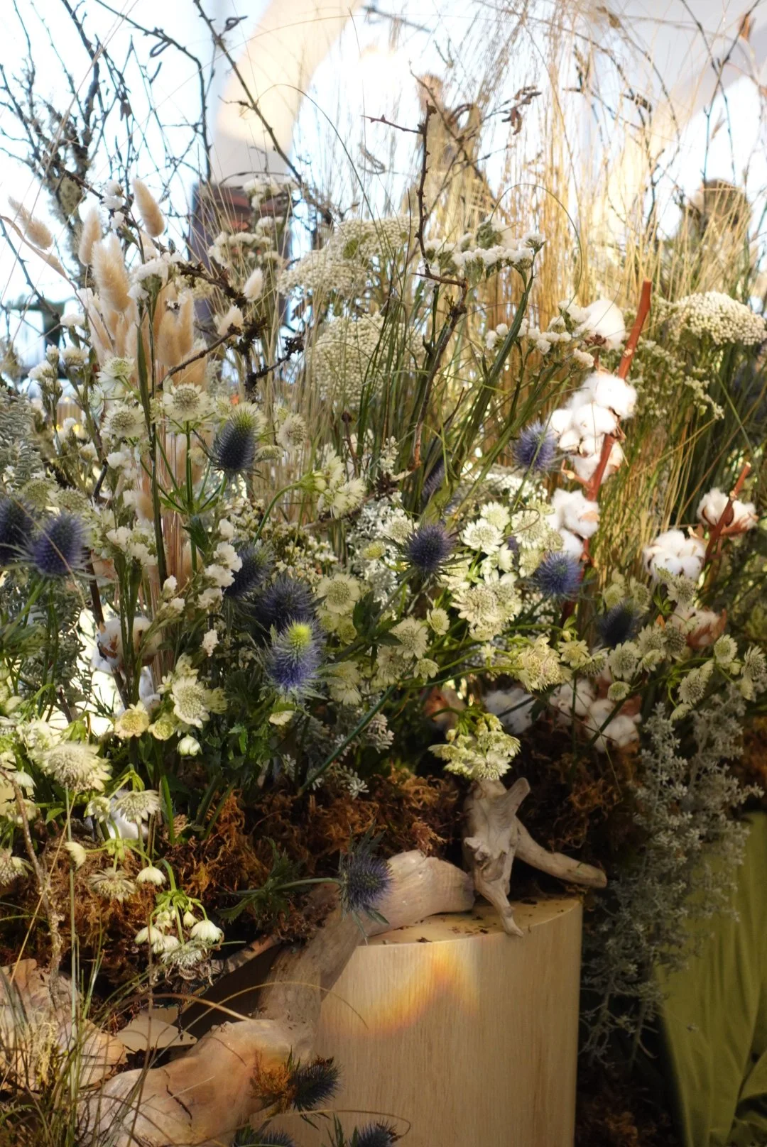 Arrangement of dried and fresh wildflowers and grasses in a vase, featuring white, purple, and brown tones.