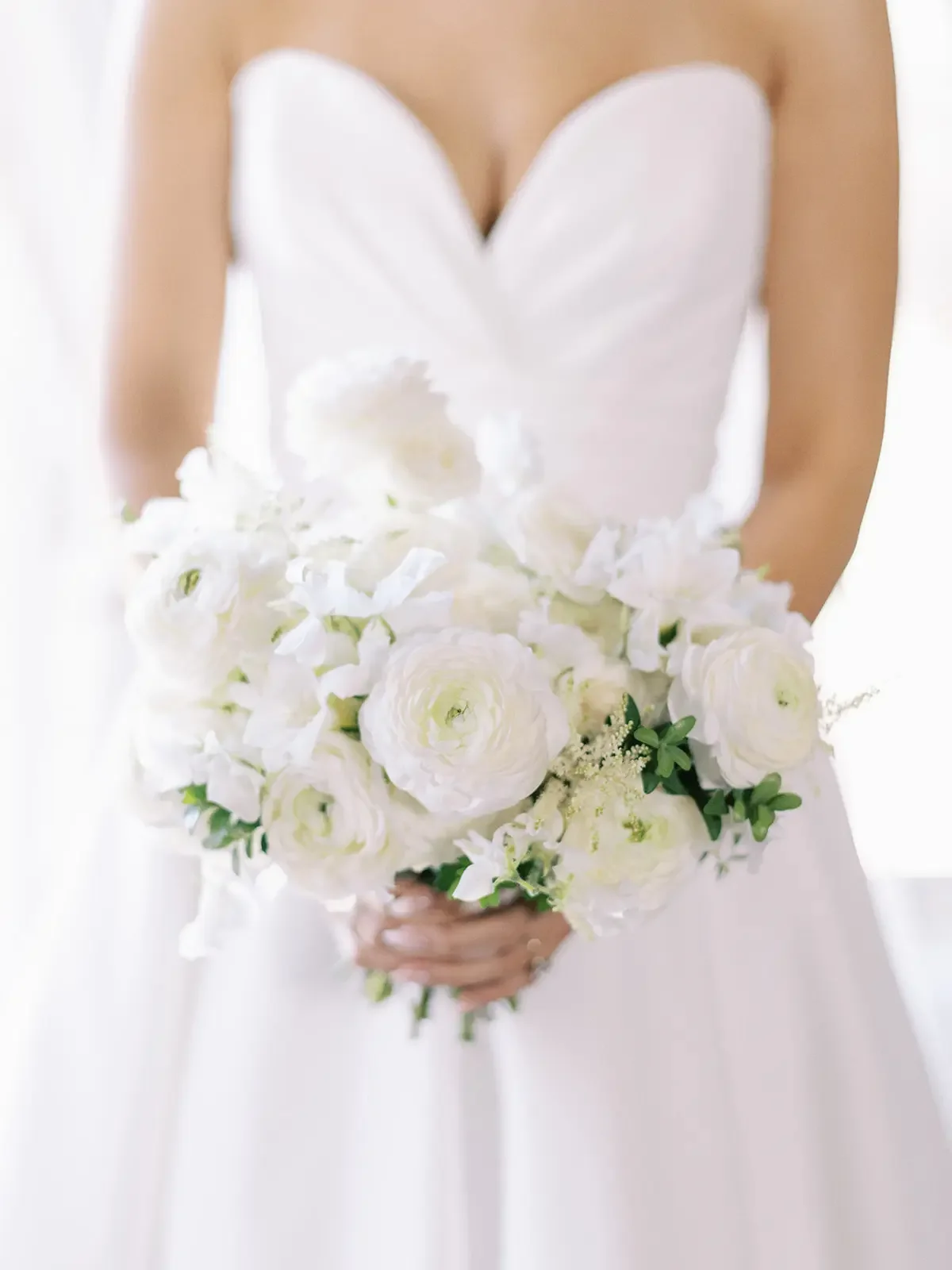 A woman in a white strapless dress holding a bouquet of white flowers.