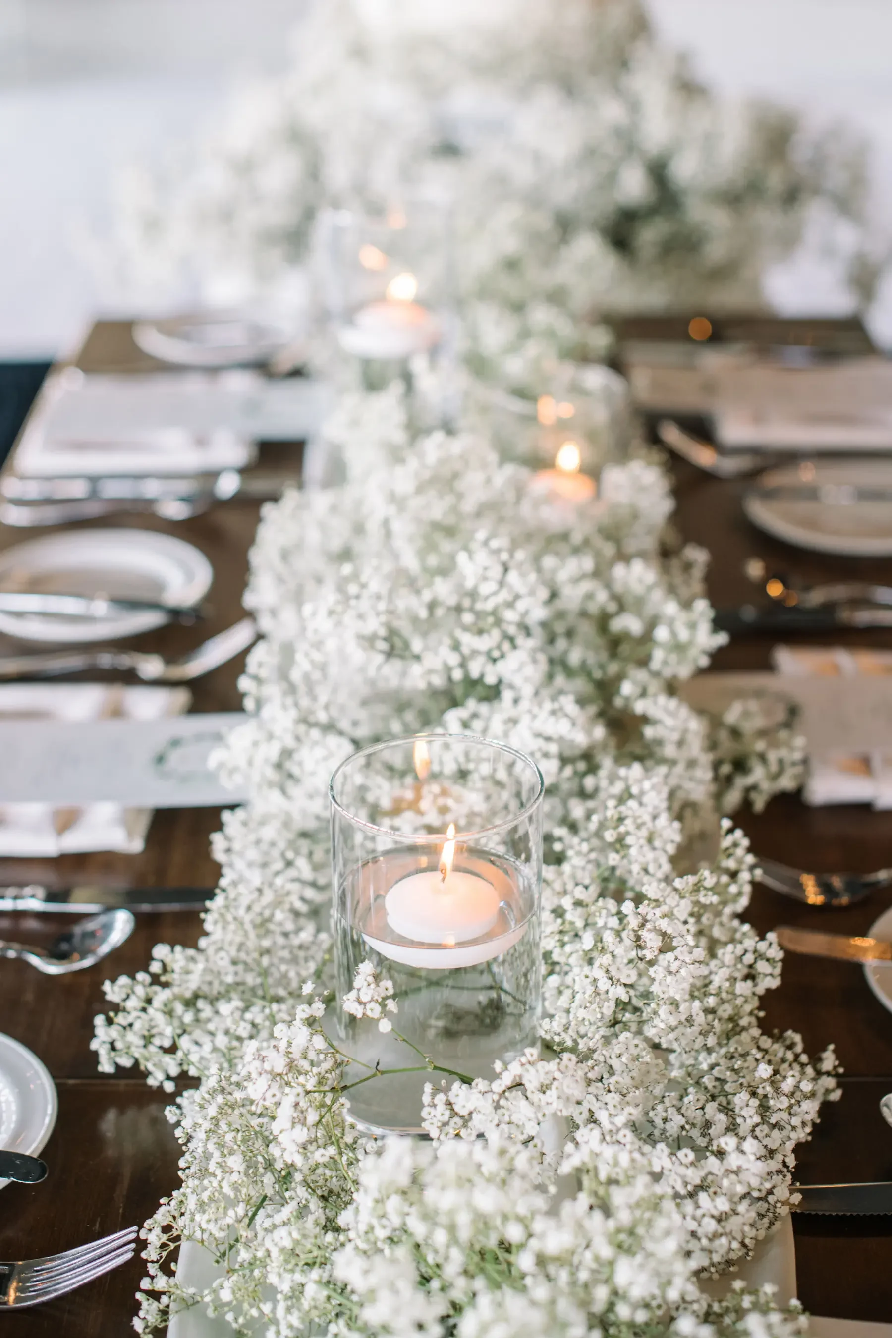 A dinner table decorated with white flowers and floating candles in glass holders.