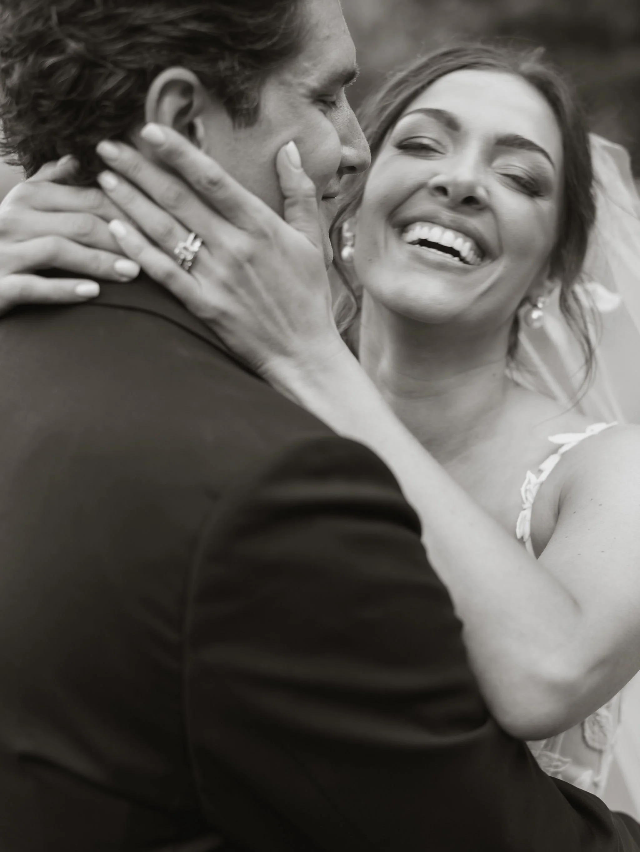 A woman and a man are smiling and embracing each other closely, woman with eyes closed and smiling broadly, woman has a wedding ring on her finger.