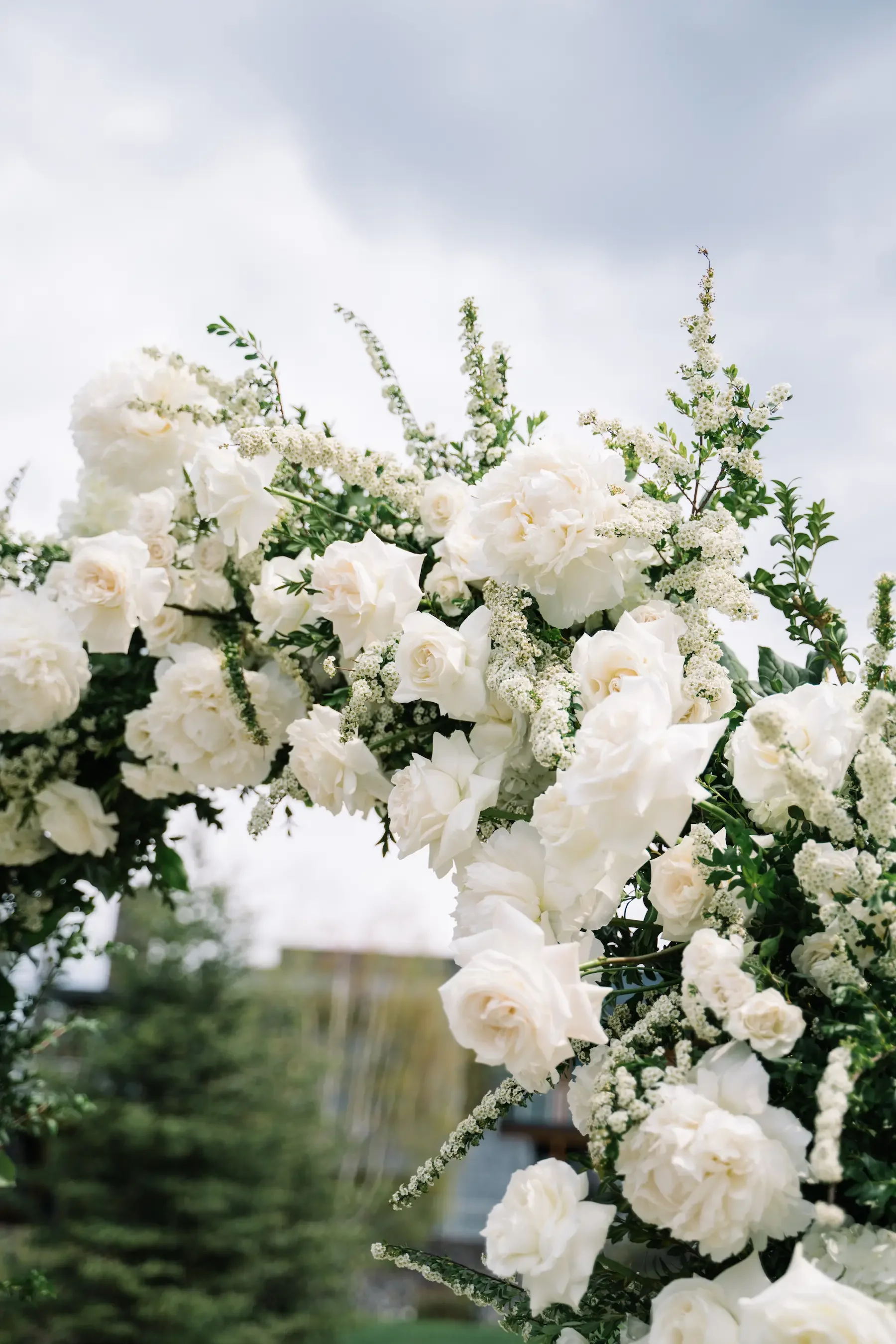 Close-up of a white floral arrangement with roses and other white flowers, set outdoors against a partly cloudy sky.