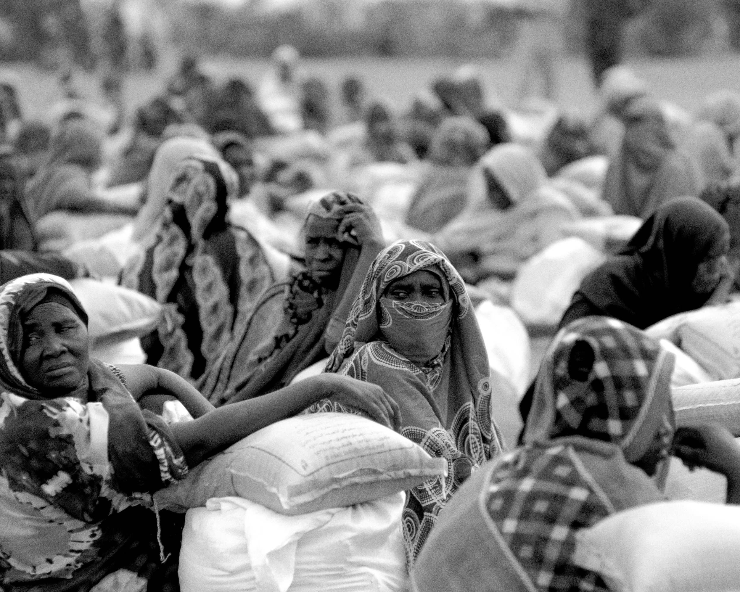 Women, displaced from war, wait to be able to leave with their food parcels in the Hotash refugee camps.