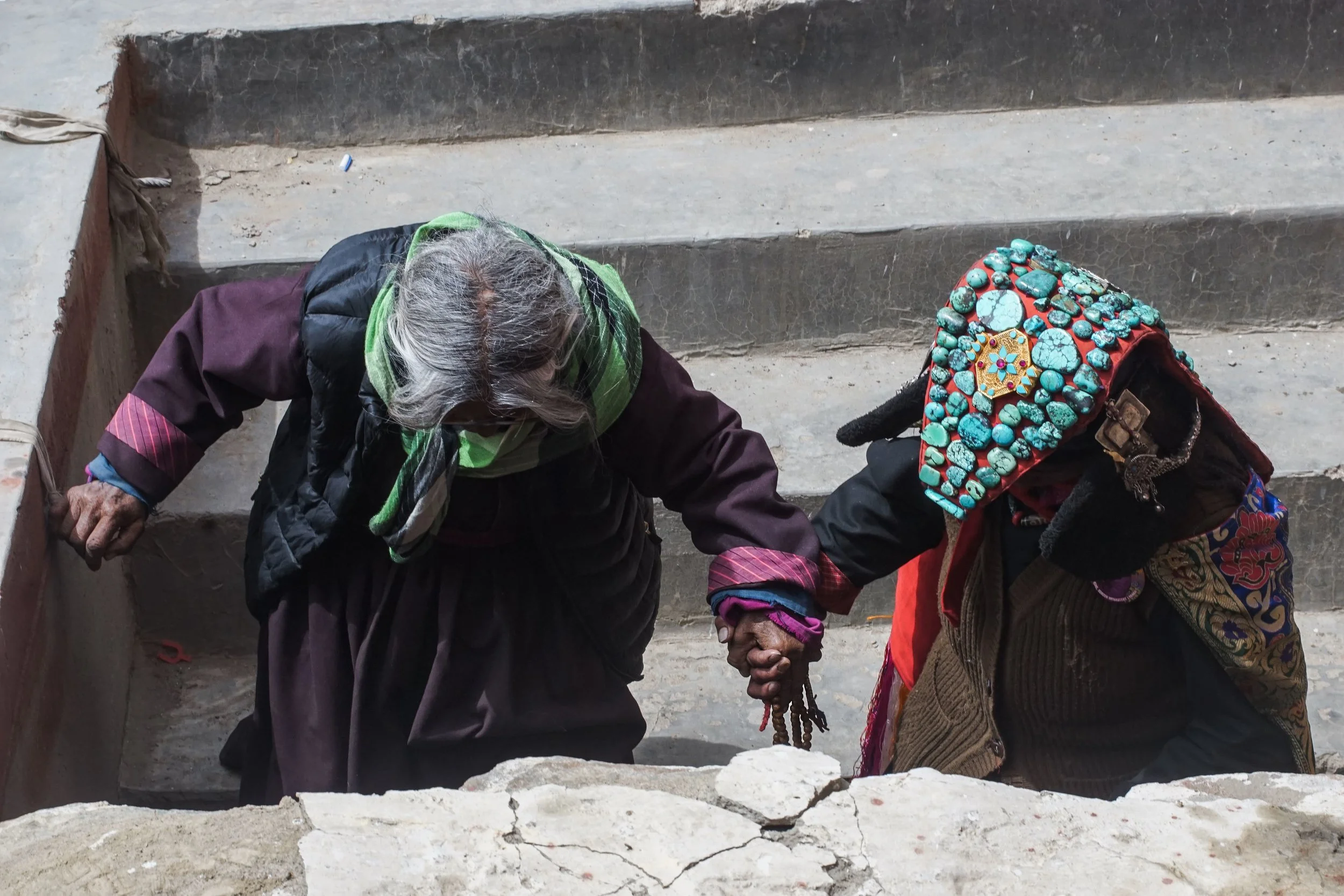 Changpa woman wearing traditional Ladakhi attire assists elder during local Buddhist festival.