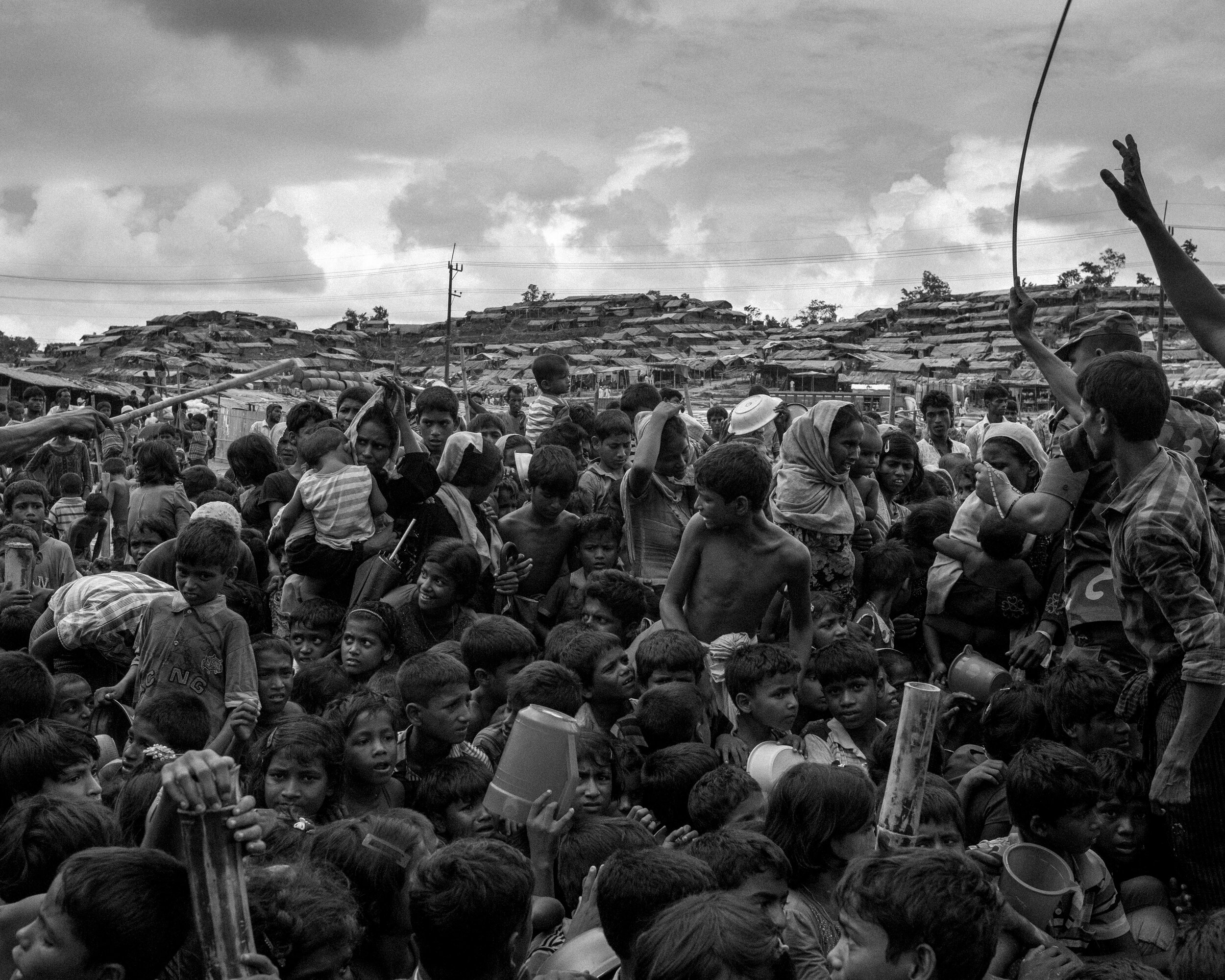   Soldiers aided by several Rohingyas try to control the distribution and try to get the crowd to sit down to calm tensions.  